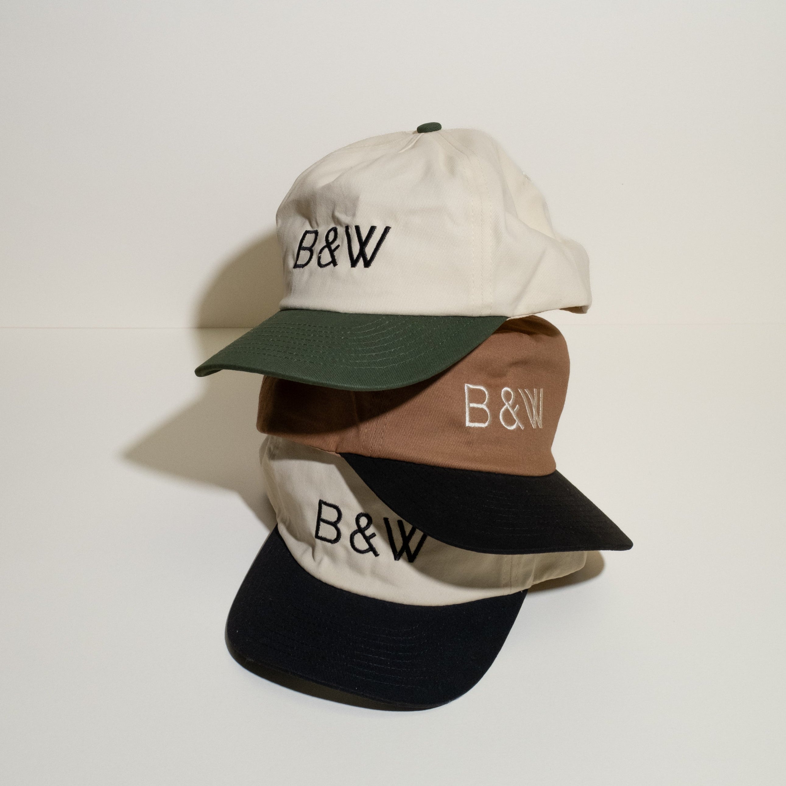 Stacked B&W Two Tone Hats with embroidered logo, featuring off-white, brown, and contrasting brims. Includes adjustable snapback closure and mesh insert liner.