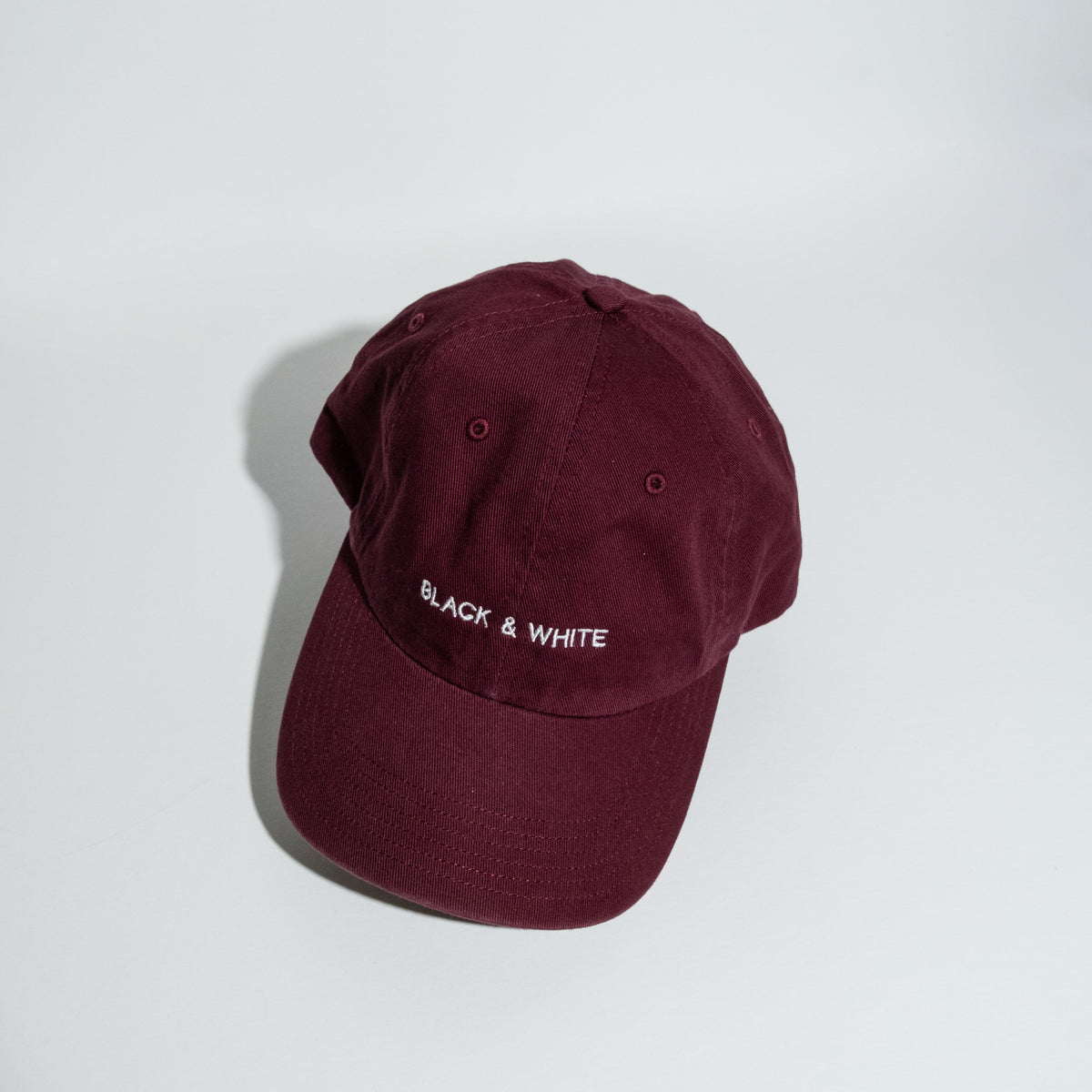 A maroon cotton baseball cap with 'BLACK & WHITE' embroidered in white on the front, photographed on a clean white background.