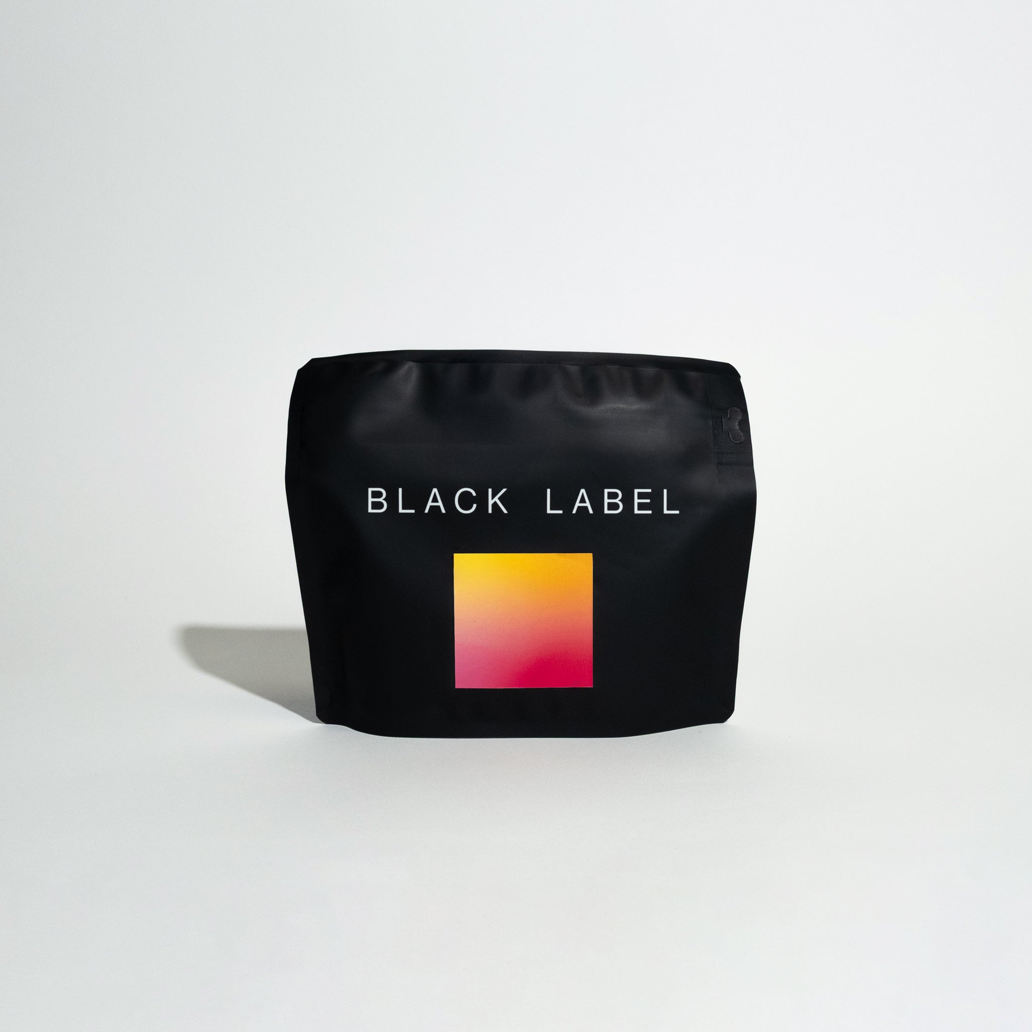 Matte-black stand-up pouch labeled BLACK LABEL with gradient square graphic, promoting coffee R - Gesha Village - Lot 50, emphasizing producer trust and sipping experience.