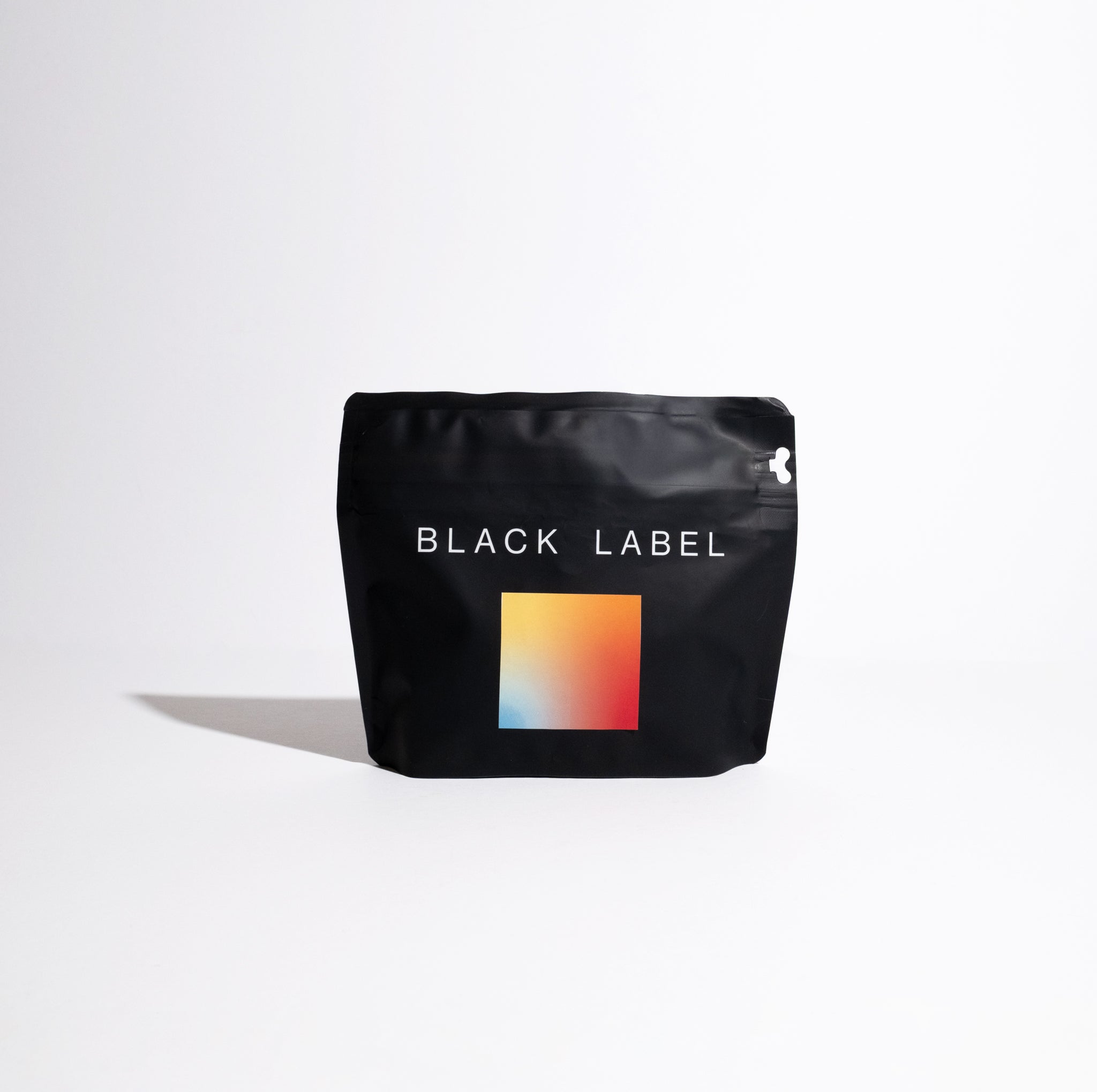 Matte-black pouch labeled BLACK LABEL, featuring gradient square graphic, represents Janson Natural Gesha - Lot 914, highlighting Janson Farms' coffee legacy.