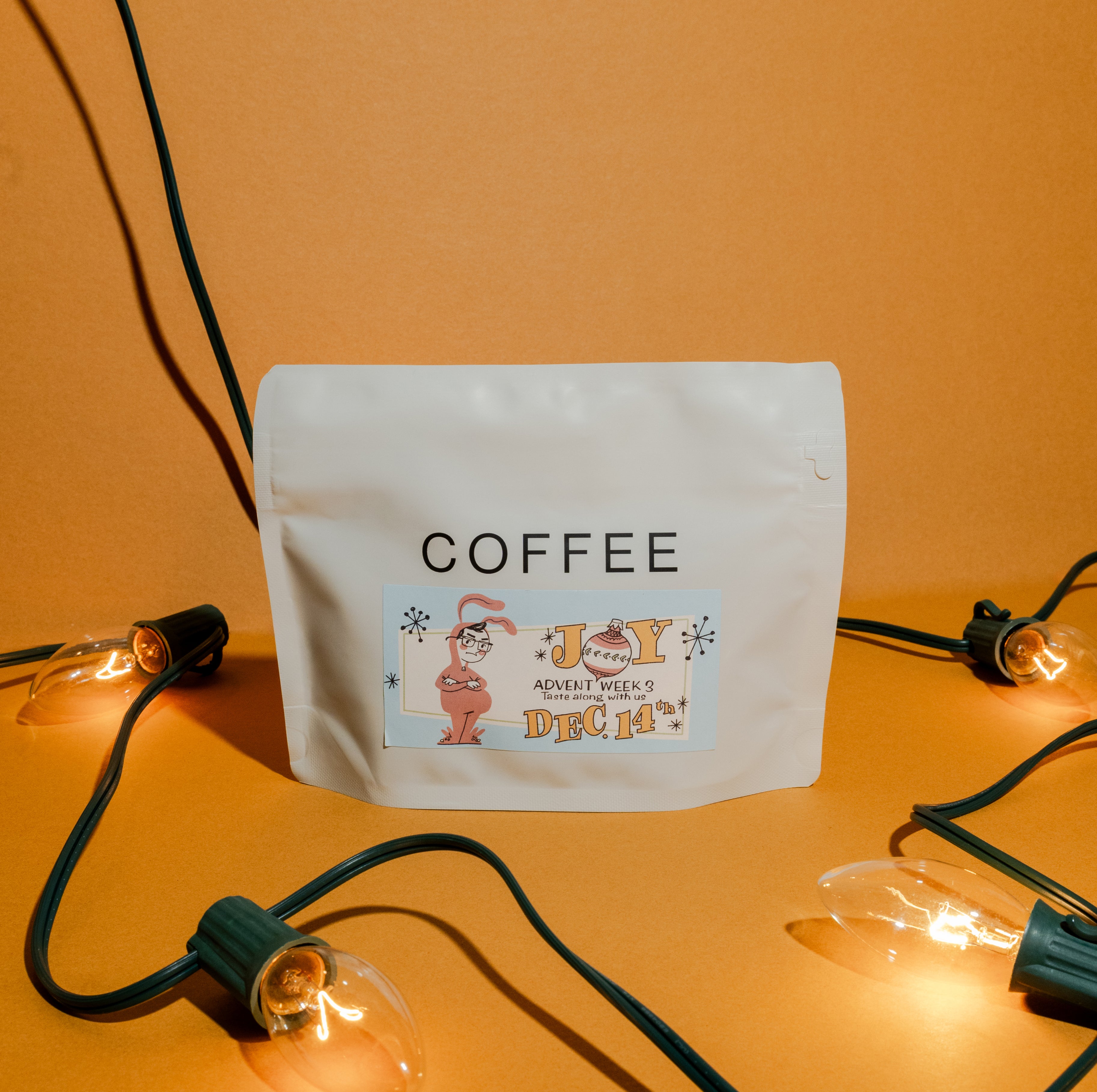 2025 B&W Advent Calendar coffee pouch, labeled “COFFEE,” features a holiday sticker with a bunny, set against vintage-style lightbulbs.