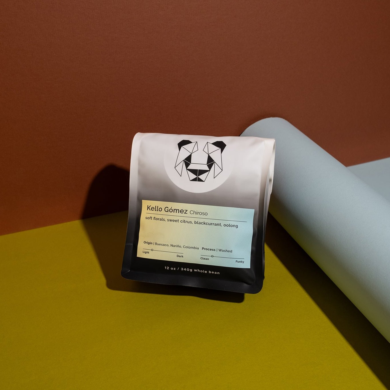 A bag of coffee on a backdrop with a yellow to blue label. The label has the title Kello Gomez Chiroso on it and the tasting notes of soft florals, sweet citrus, blackcurrant and oolong.