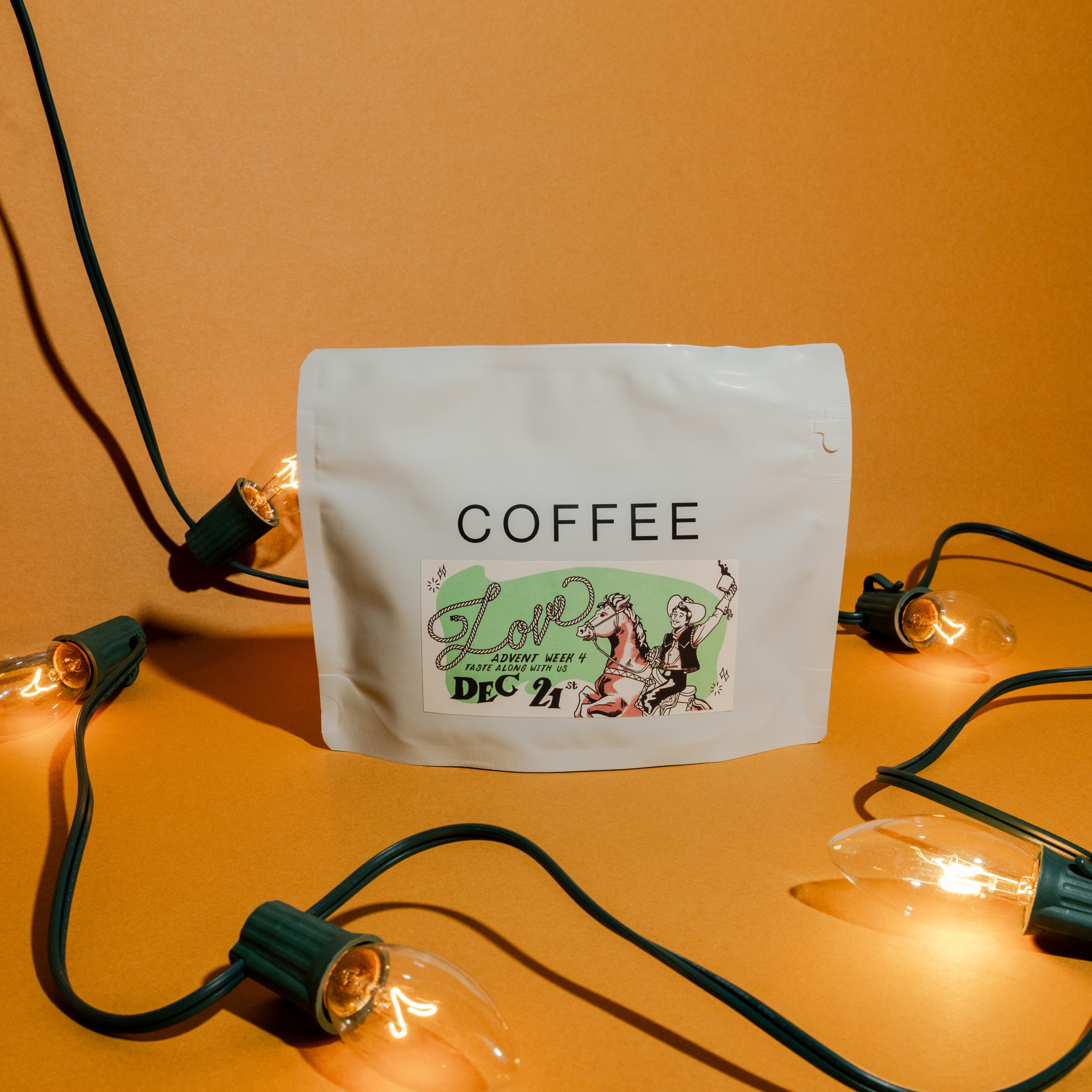 2025 B&W Advent Calendar coffee pouch with holiday sticker, surrounded by lit string lights, inviting tasting on December 21st.