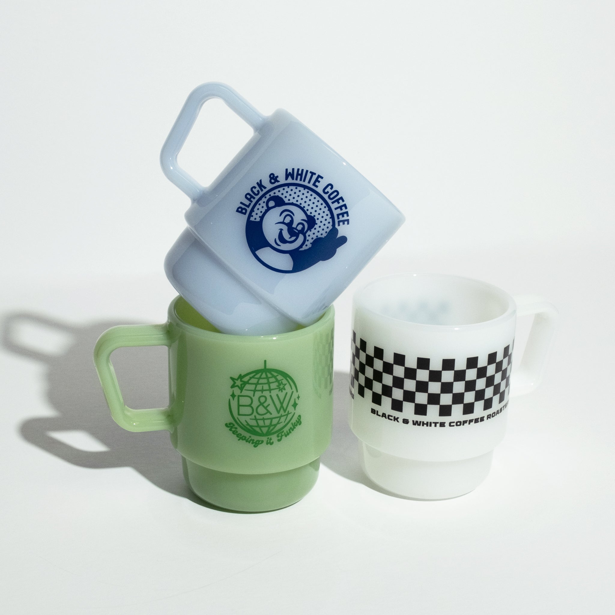 B&W Milk Glass Mugs, stacked top with bear icon, middle globe logo, right white with checkerboard band. Vintage-inspired, versatile, and stackable design.