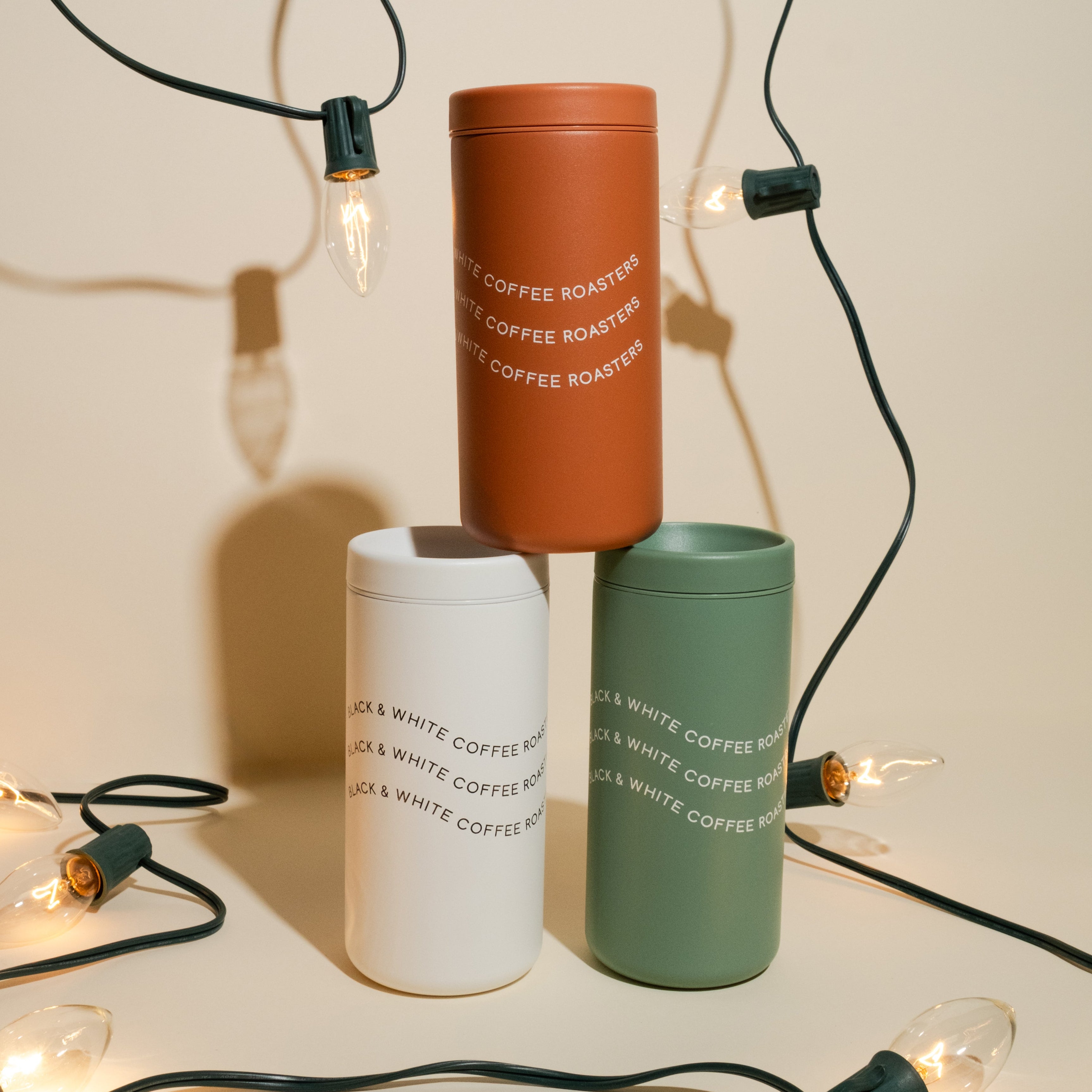 Three traveler cups stacked on top of each other on a holiday themed backdrop with lights.