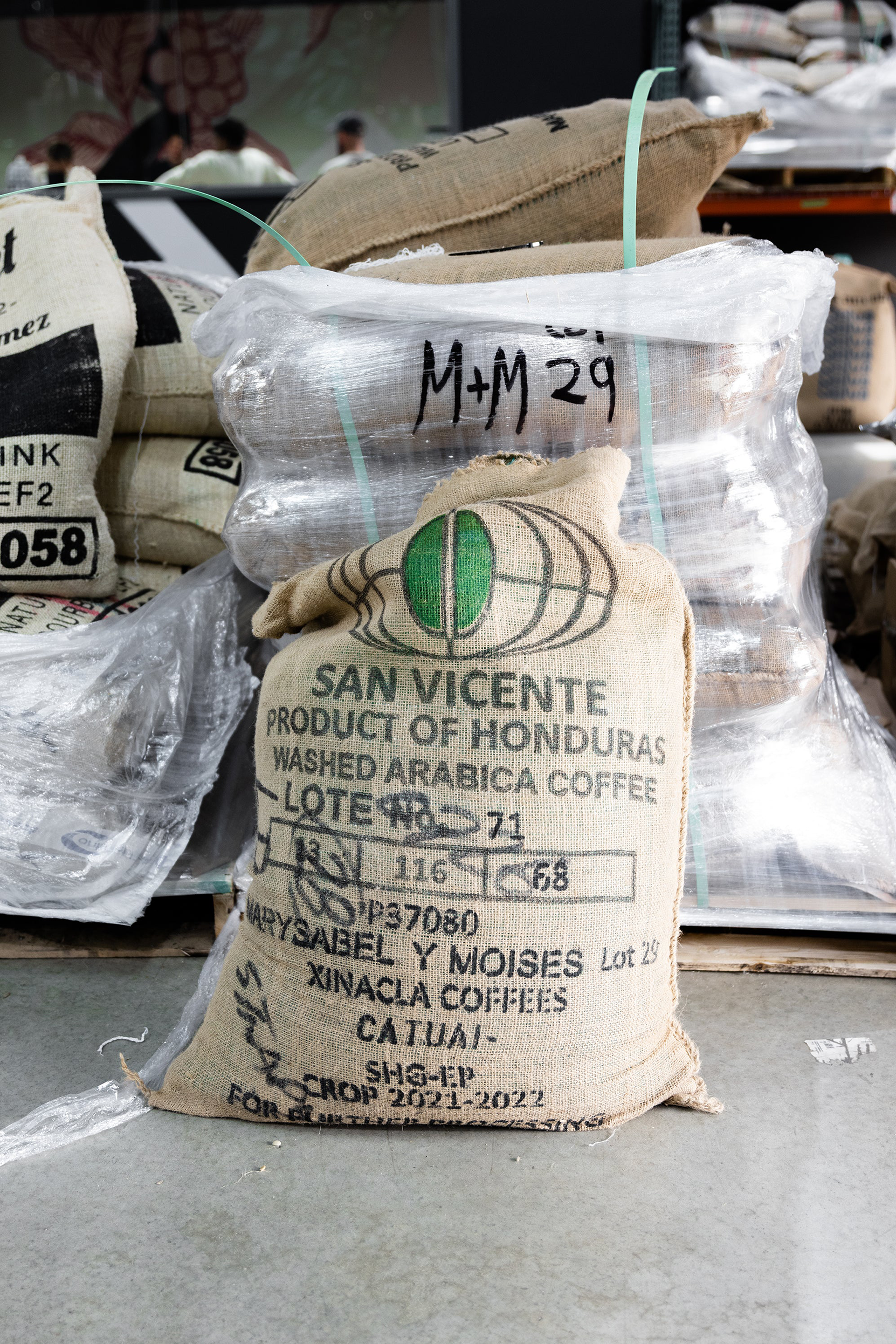 A bag of green coffee in a jute bag sitting on the floor of a warehouse with the words, San Vincente, Product of Honduras washed Arabica coffee on them.