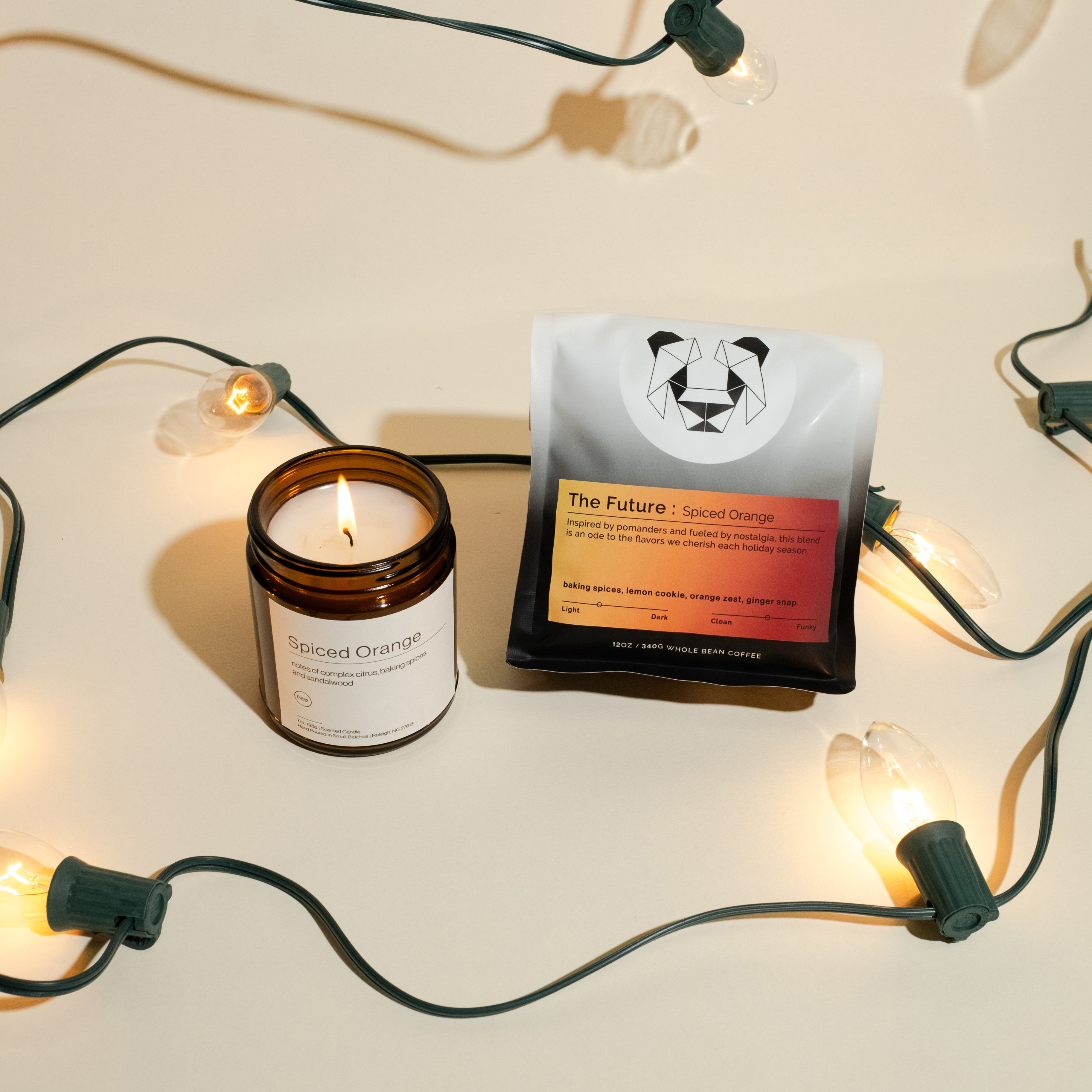 Spiced Orange Coffee + Candle set, featuring an amber jar candle and whole-bean coffee, surrounded by clear holiday lights.