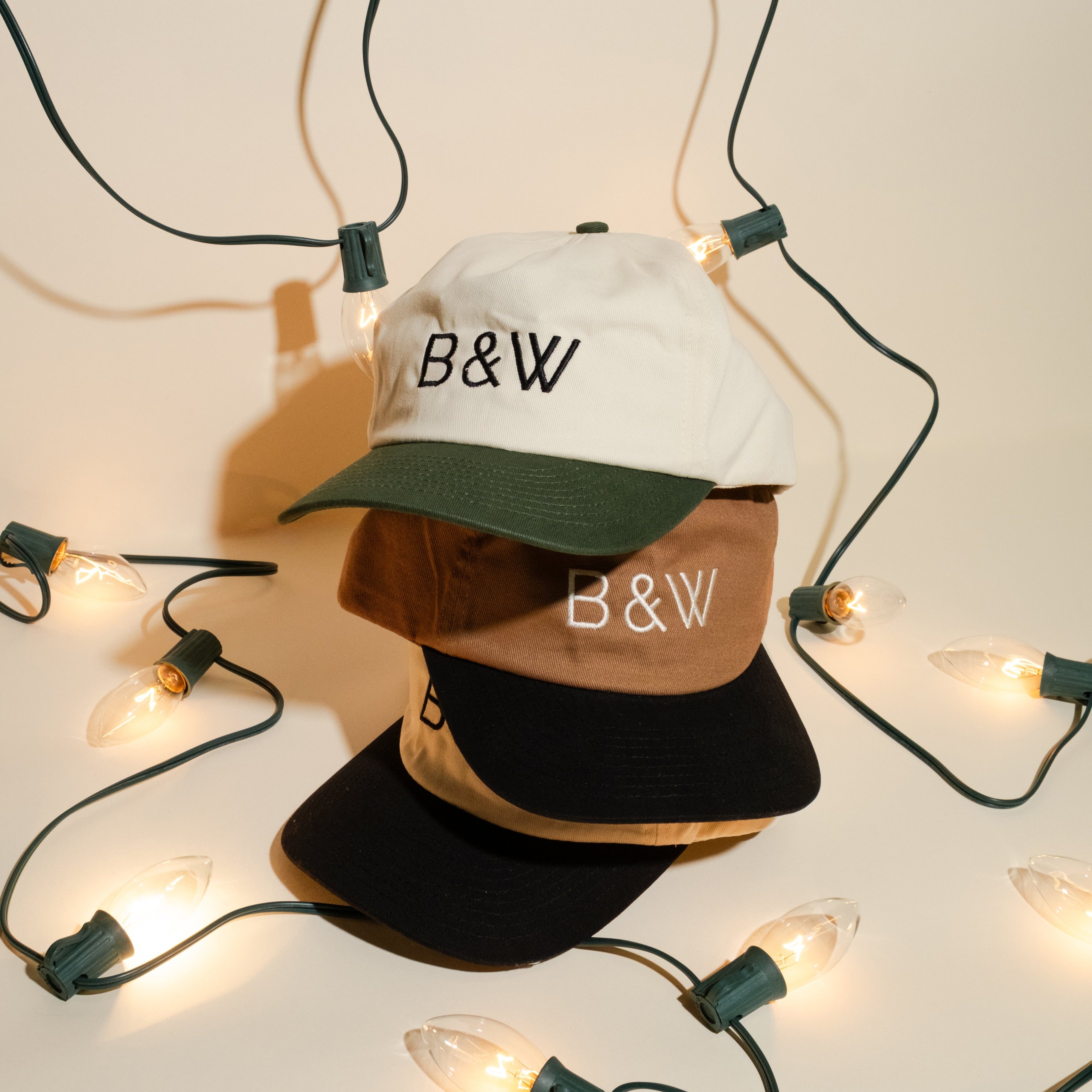 B&W two toned cotton dad hats stacked on top of each other with a holiday themed backdrop with Christmas lights.