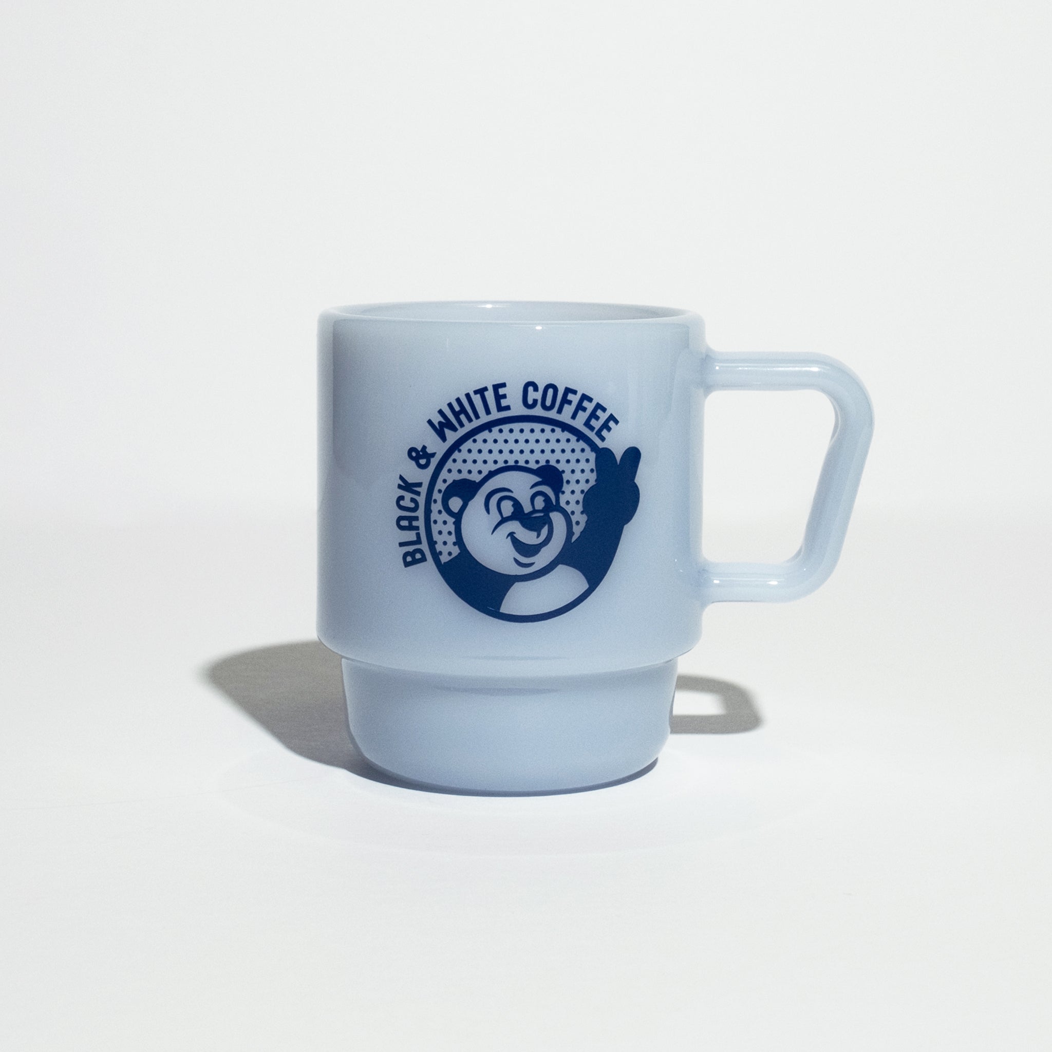 B&W Milk Glass Mug featuring a smiling bear graphic with peace sign, designed for hot or cold drinks, stackable, and boasting a classic milk glass look.