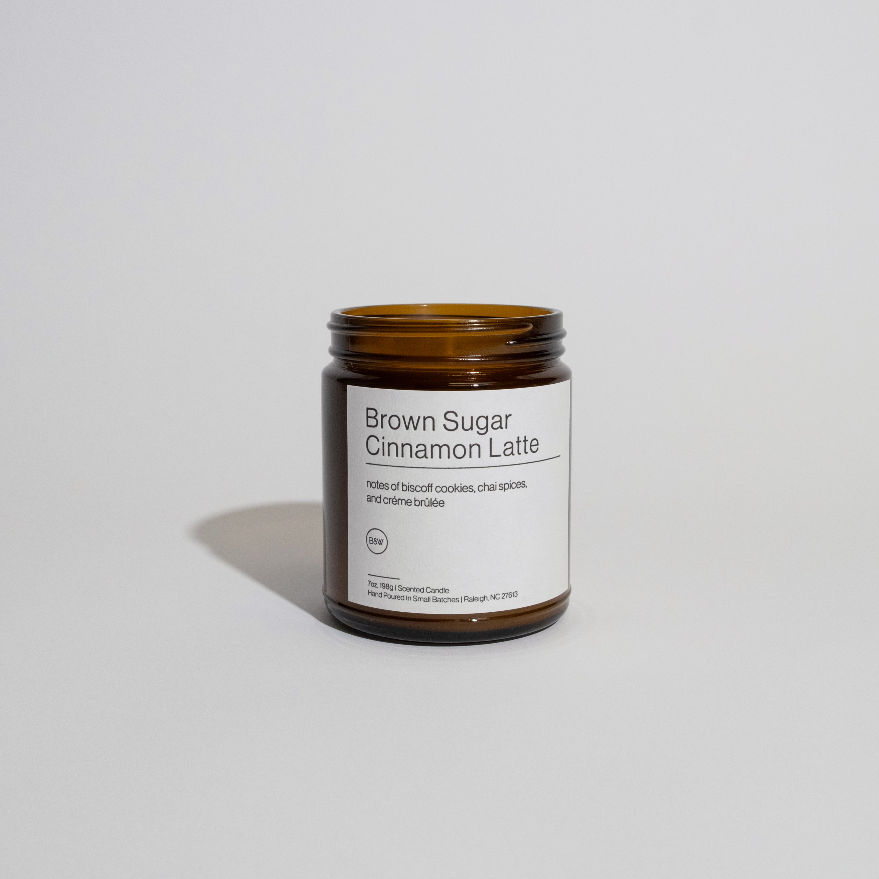 B&W Winter Candle: Amber-brown glass jar with Brown Sugar Cinnamon Latte label, featuring biscoff, chai, and crème brûlée scents; hand-poured, 7 oz, 30-hour burn time.