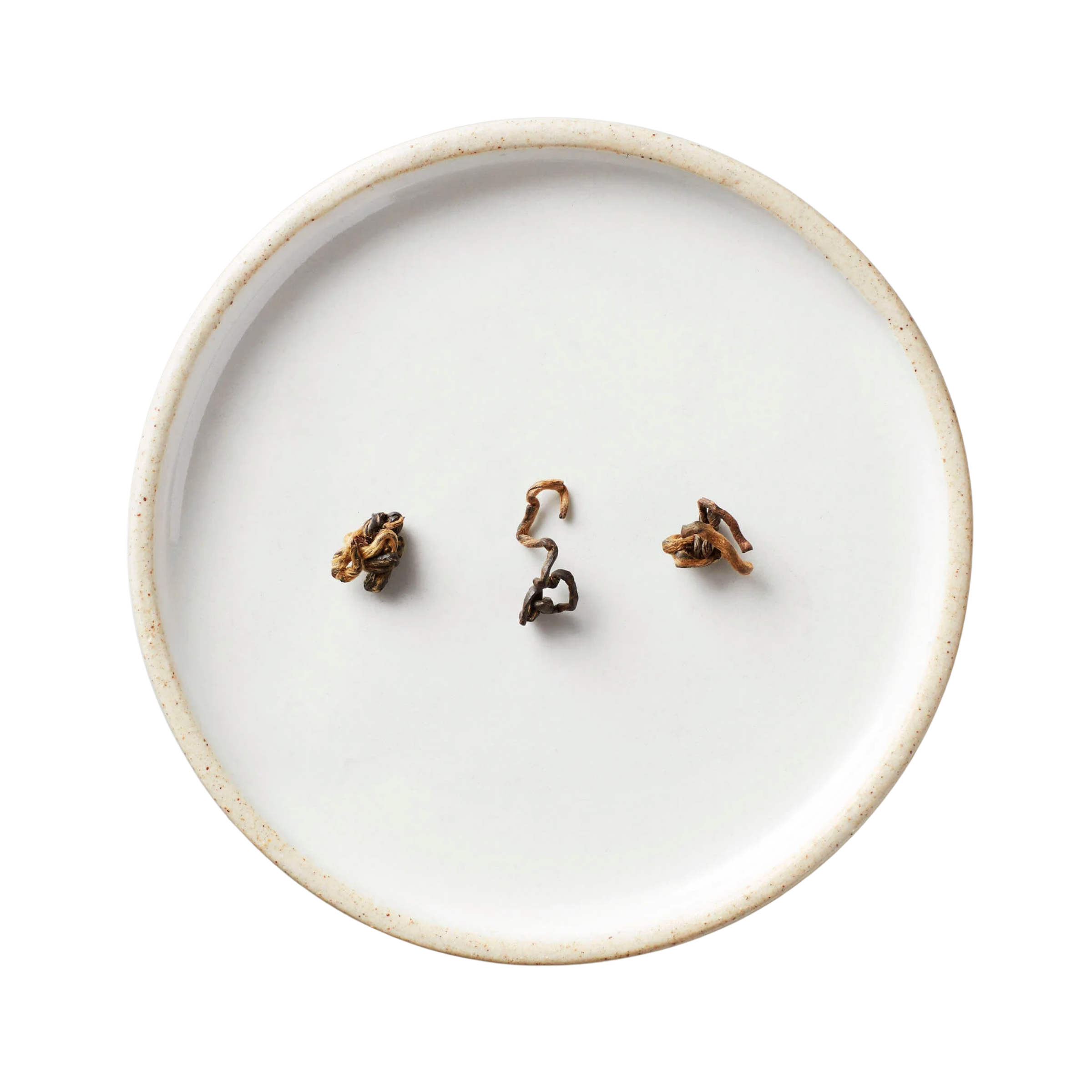 White ceramic plate displaying twisted, brown-and-gold hand-rolled tea leaves, showcasing Hugo Tea's Gao Wen black tea from Yunnan, distinguished by its high-heat roasting process.