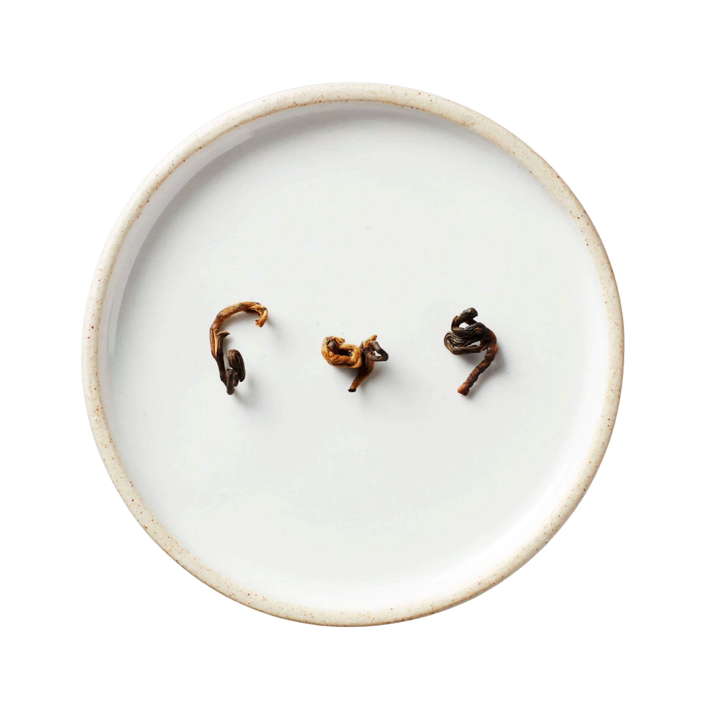 Hugo Grey | Black Blend tea leaves, dark brown with golden tips, rest on an off-white ceramic plate with a speckled rim, showcasing quality Yunnan tea.
