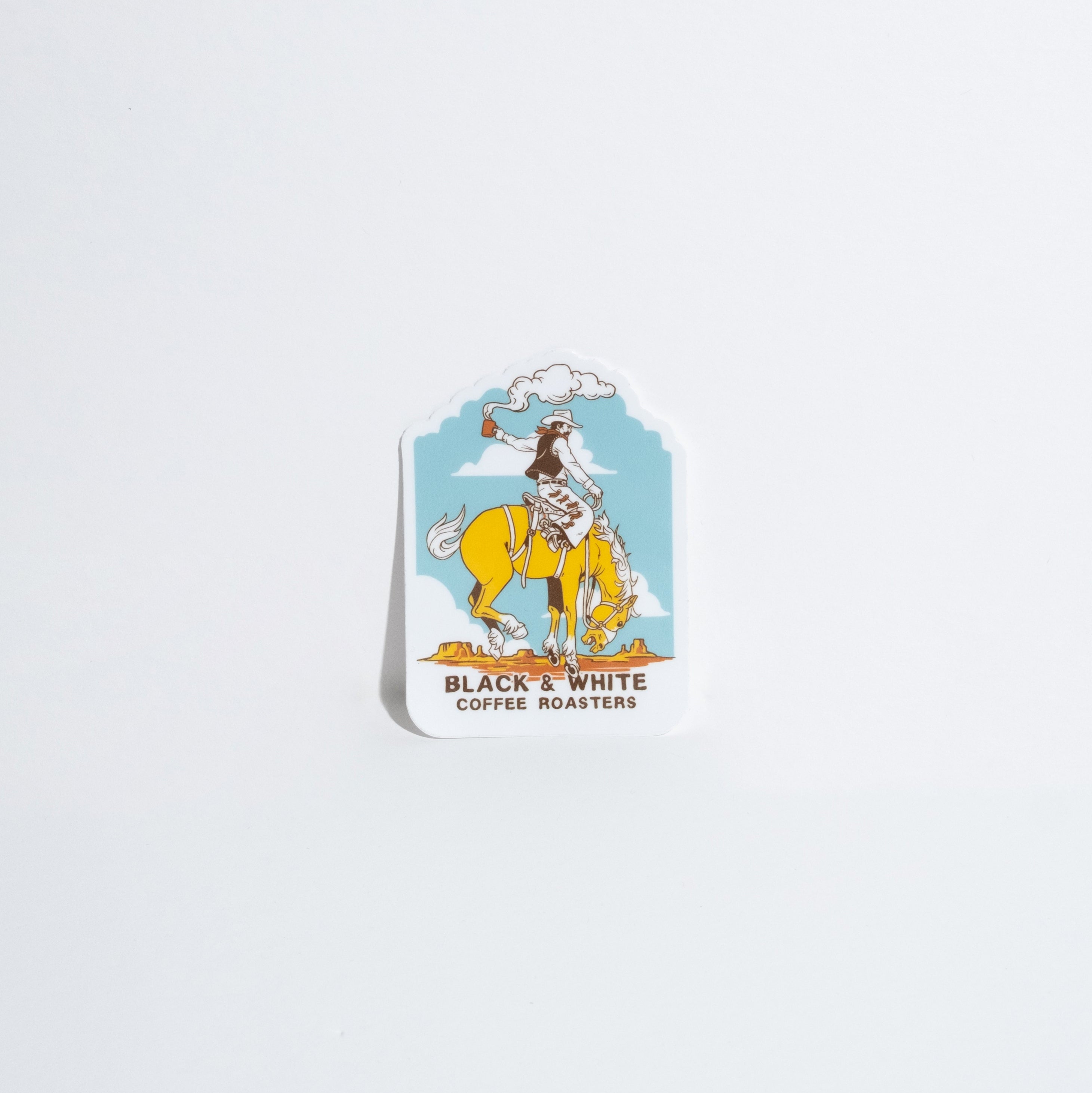 A die-cut sticker featuring a cowboy riding a yellow horse against a light blue sky, with the text 'BLACK & WHITE COFFEE ROASTERS' below the illustration, shown on a plain white background.