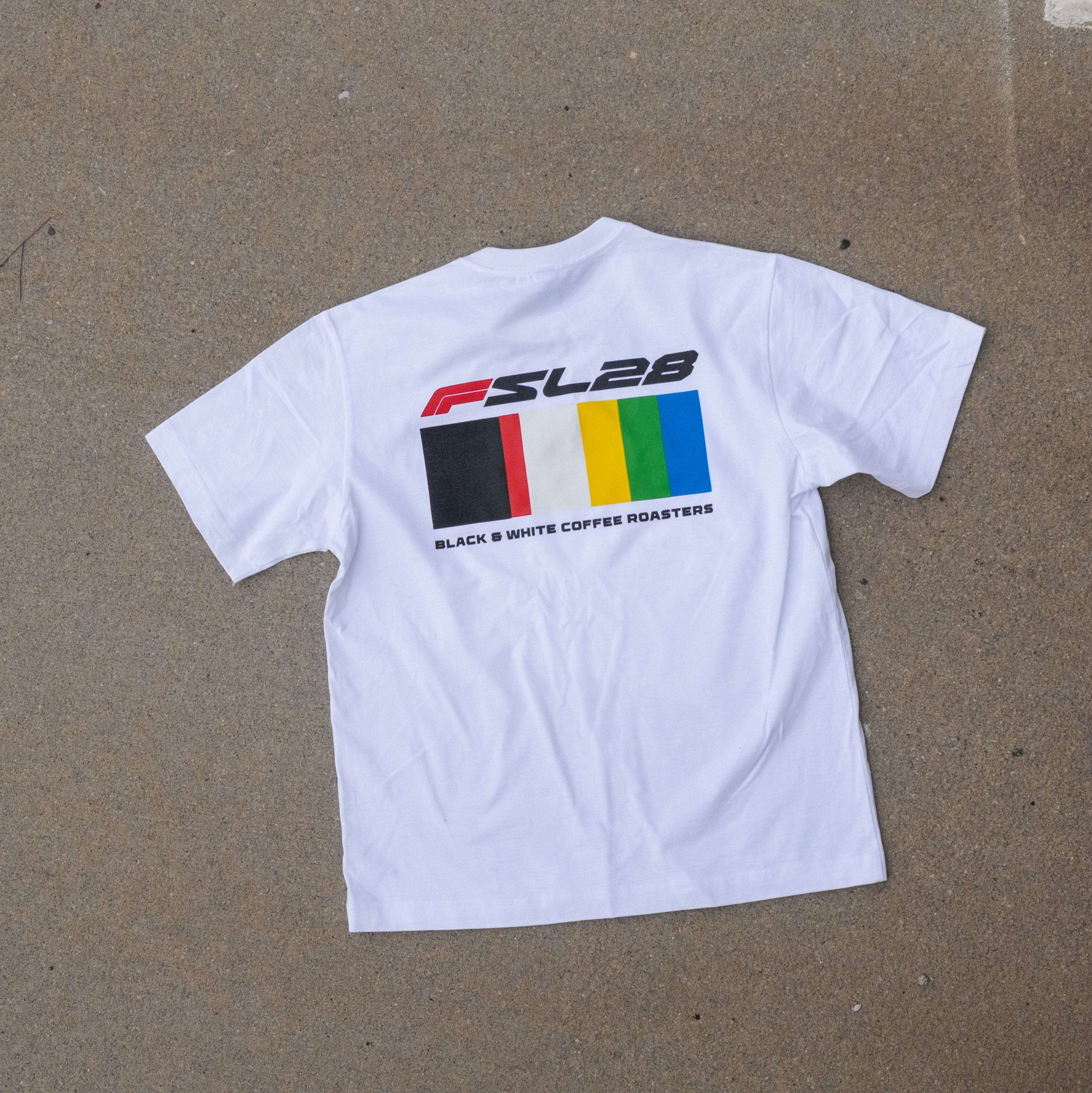 Color Bar Birthday Shirt featuring FSL28 logo, six color blocks, and BLACK & WHITE COFFEE ROASTERS text, laid flat on textured surface.