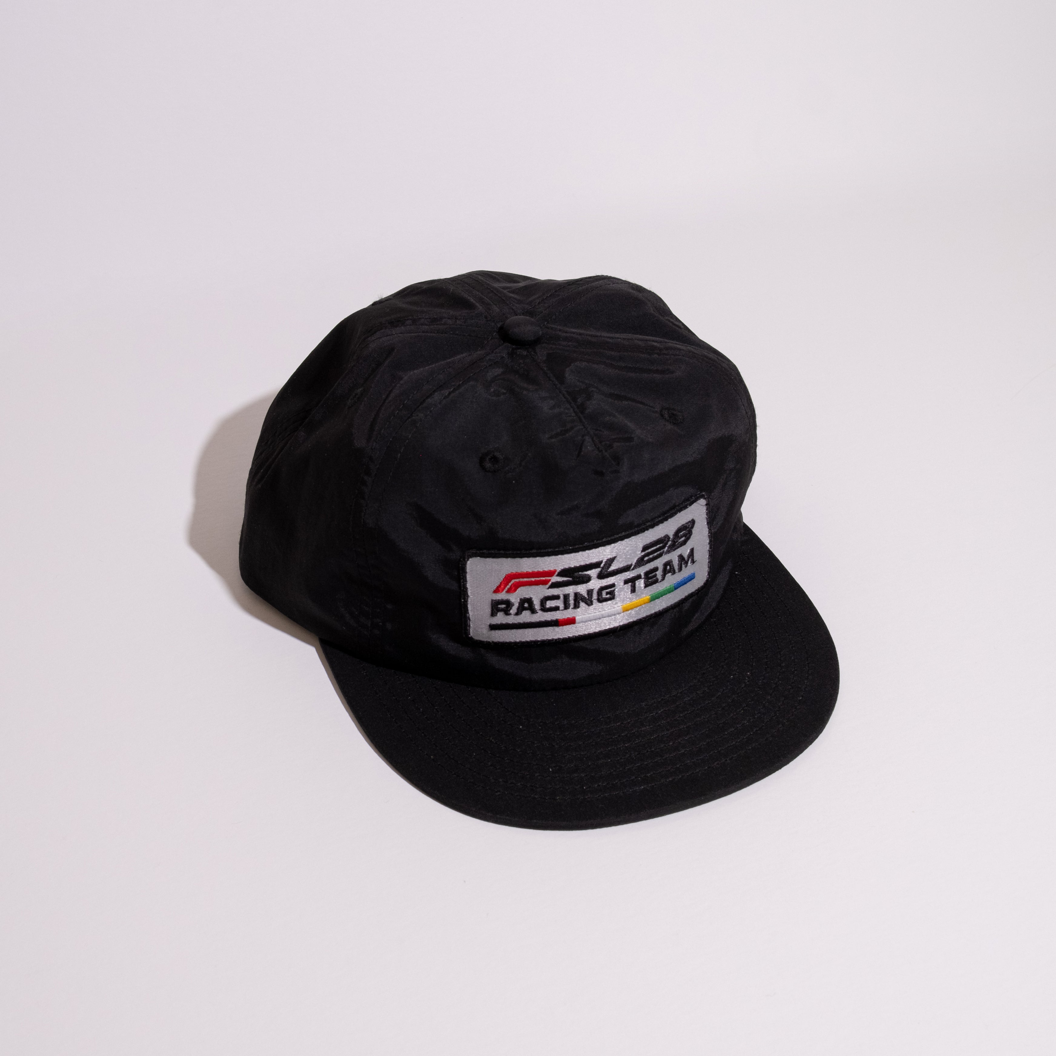 FSL28 Racing Team Hat; black cap with embroidered patch, flip-up buckram, inspired by 70s Grand Prix art. Adjustable snapback fit.