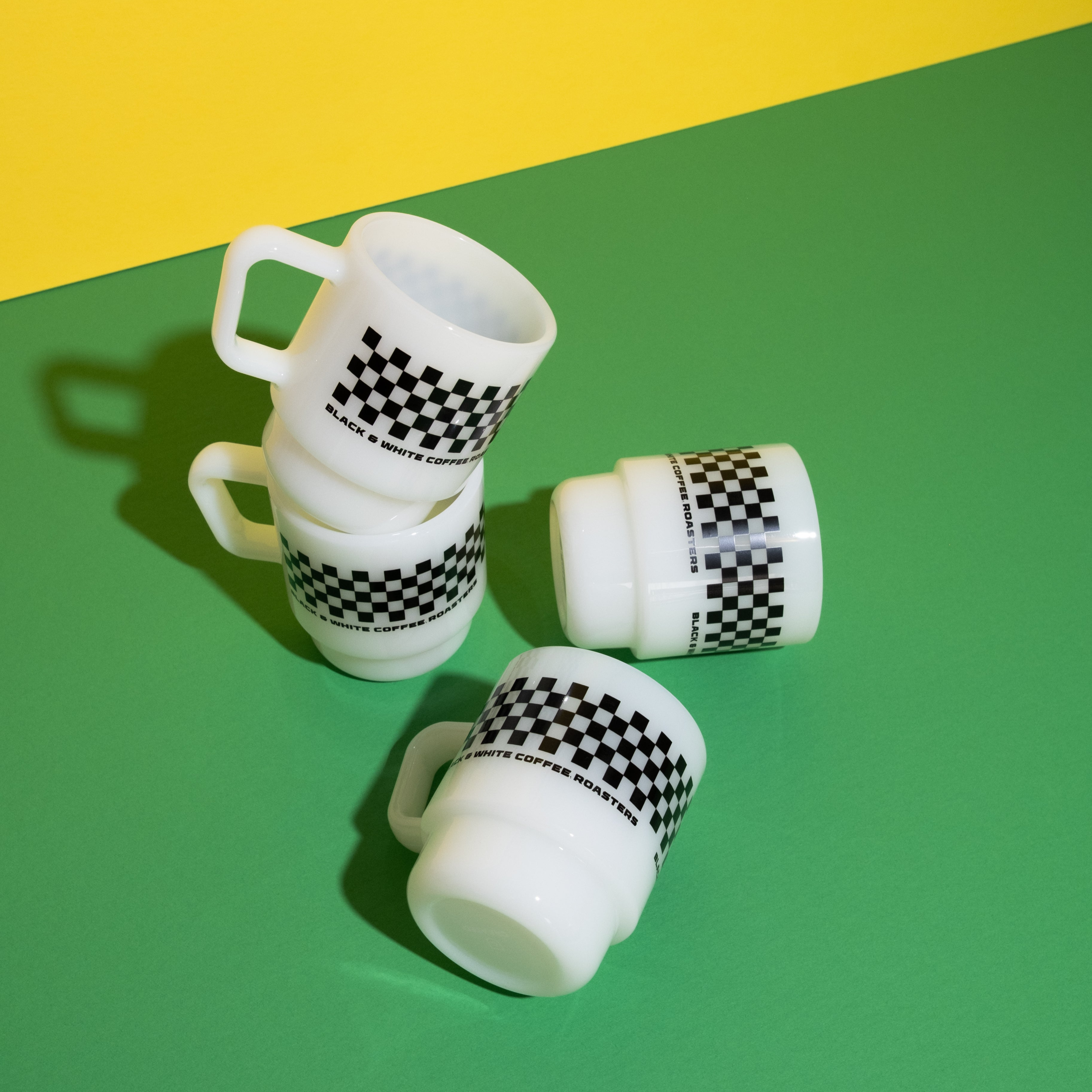White glass mugs with black checkered patterns on a green and yellow background.