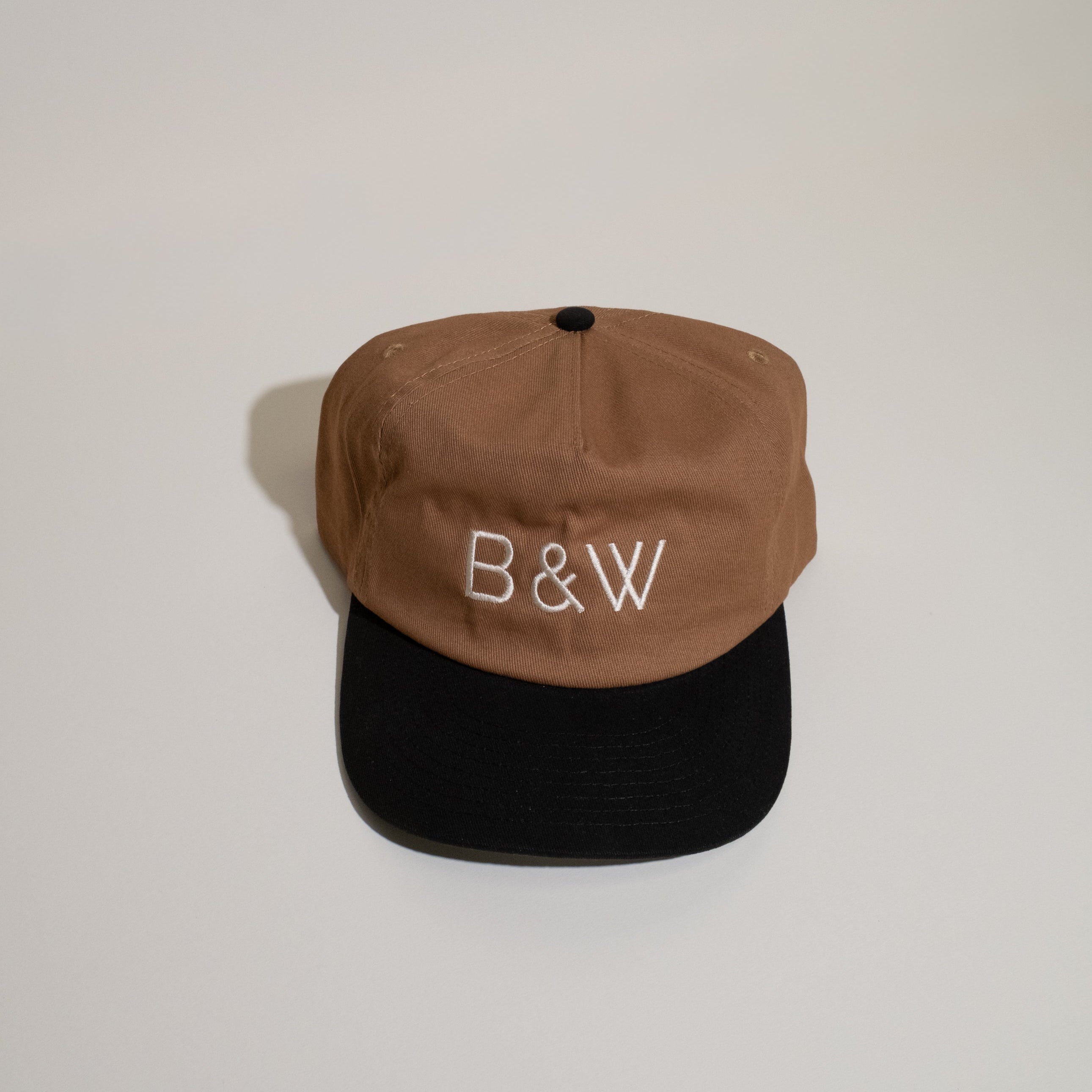 B&W Two Tone Hat featuring a brown crown and black bill, embroidered with B & W on front; includes adjustable snapback and pre-curved visor.