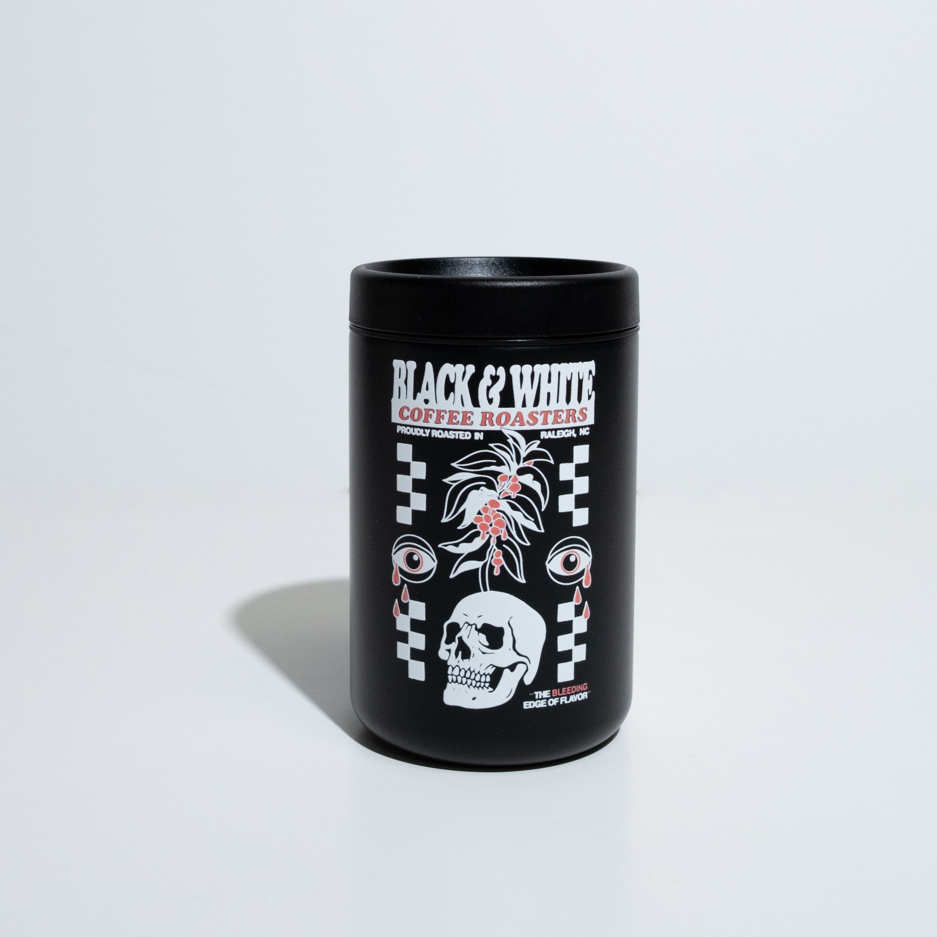 A Black 10oz travel cup with a large white and red graphic that says, "Black and White Coffee Roasters, Proudly roasted in Raleigh, NC" and "The Bleeding Edge Of Flavor." The graphic has checker board design on the left and right with a skull with a coffee tree growing out of it. The graphic is finished off two eyeballs crying red tear drops.