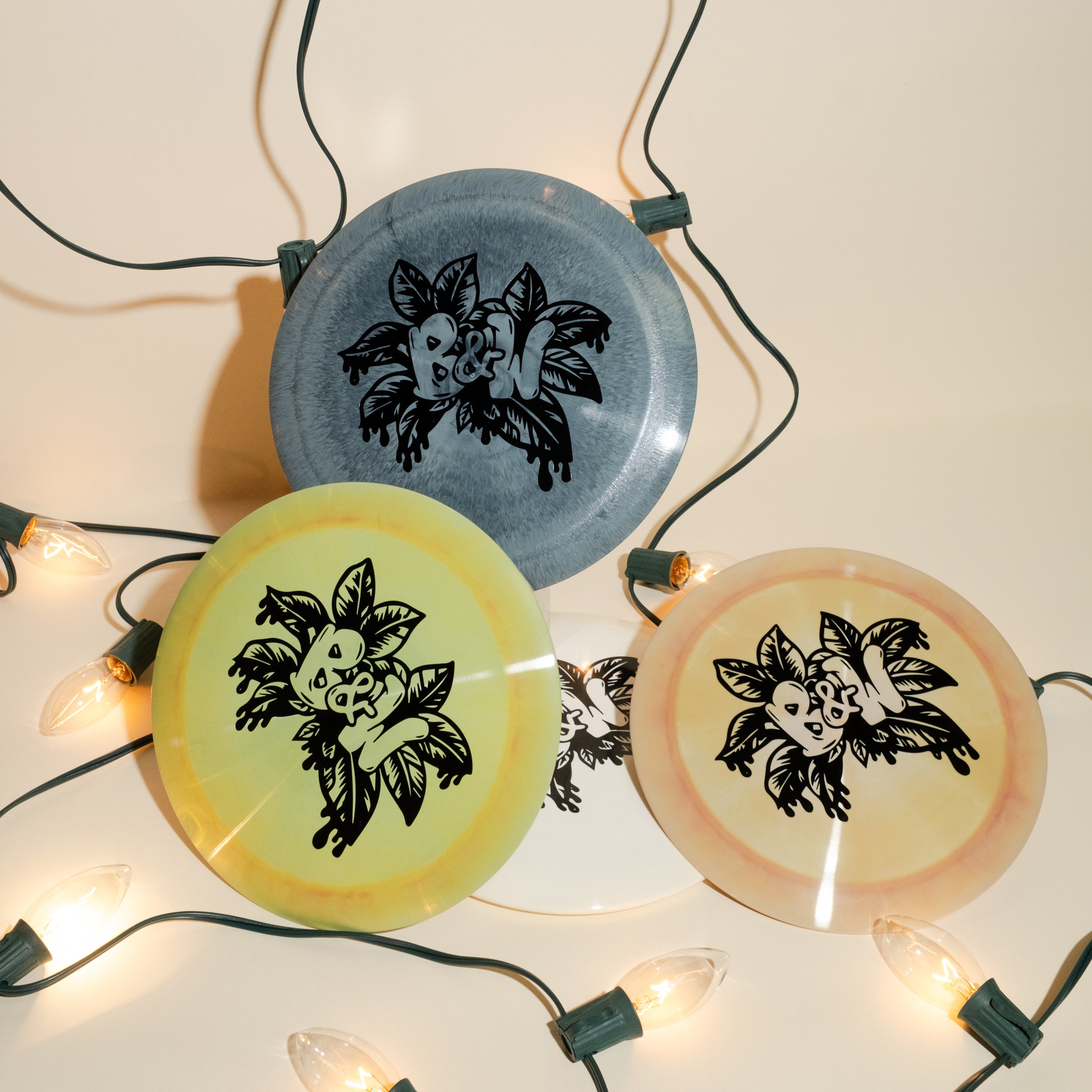 A stack of disc golf discs in different colors on a light background with holiday themed lights.