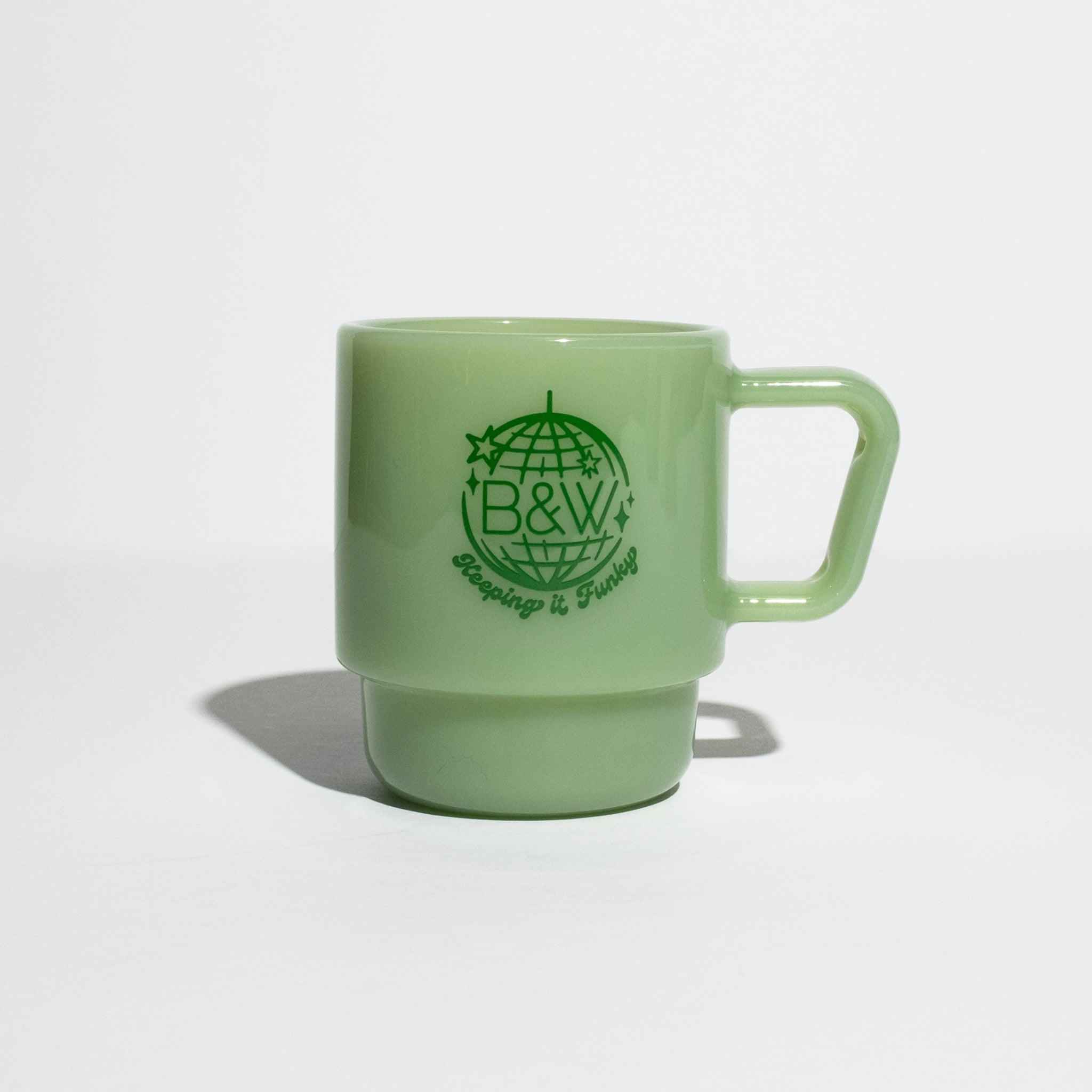 Pale green B&W Milk Glass Mug with squared handle, globe graphic, and slogan. Inspired by vintage style, perfect for hot or cold drinks.