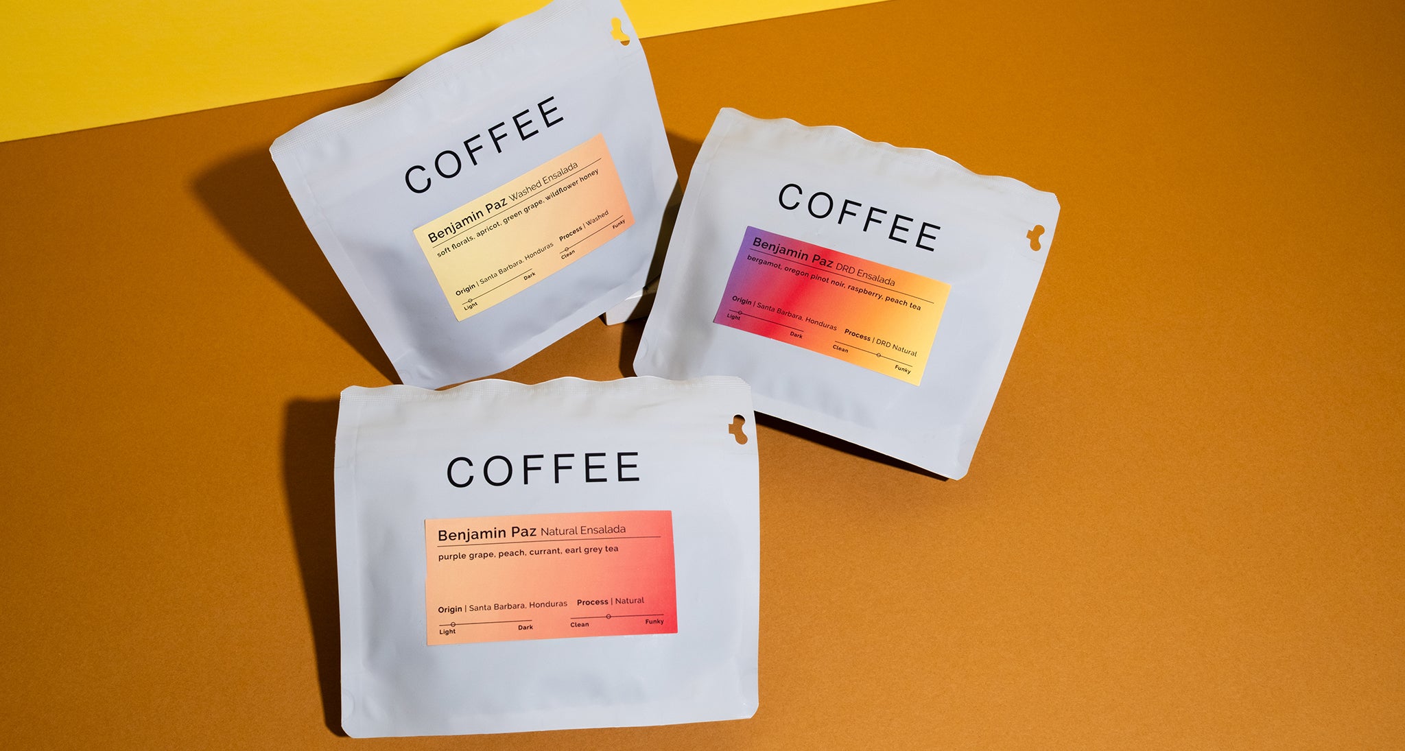 3 bags of coffee on a colorful background with three different colorful labels. Each label has Benjamin Paz Ensalada on them with different processes listed. Washed, Natural and DRD.