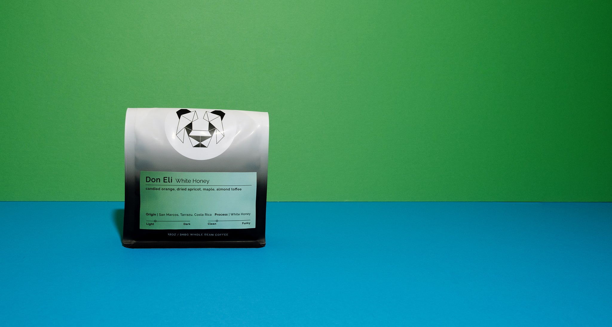 A bag of coffee on a multicolored background with a colorful gradient label that says, "Don Eli White Honey." The label has tasting notes of candied orange, dried apricot, maple and almond toffee.