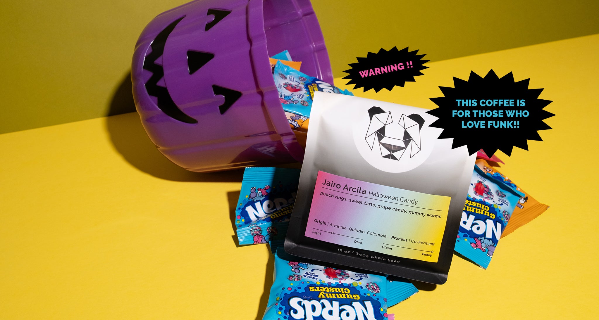 Halloween-themed coffee with candy packages on a bright and colorful background. The label says Jairo Arcila Halloween Candy with notes of peach rings, sweet tarts, grape candy, and gummy worms.