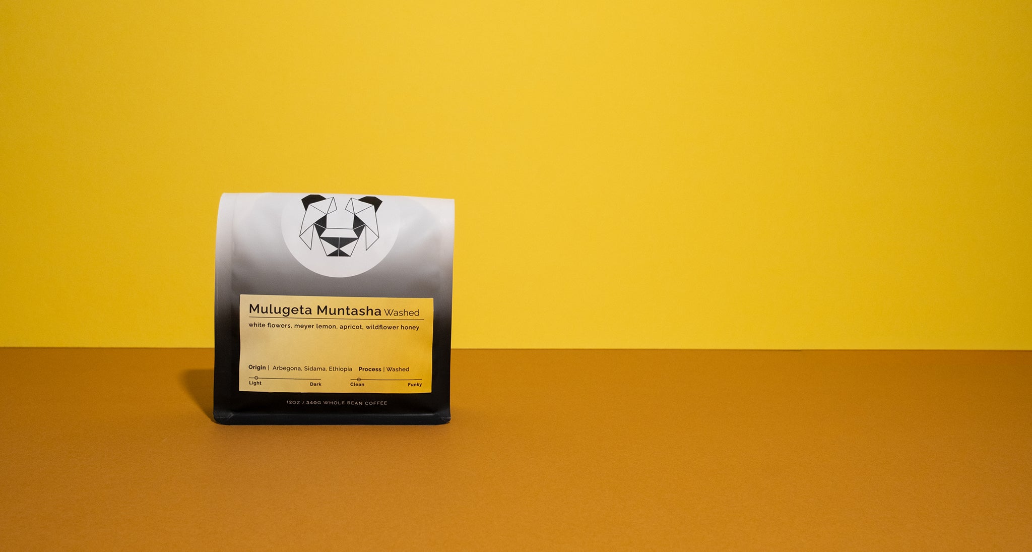 A bag of coffee on a multicolored background with a bright gradient label that says, "Mulugeta Muntasha Washed." The coffee label has notes of white flowers, meyer lemon, apricot, and wildflower honey.