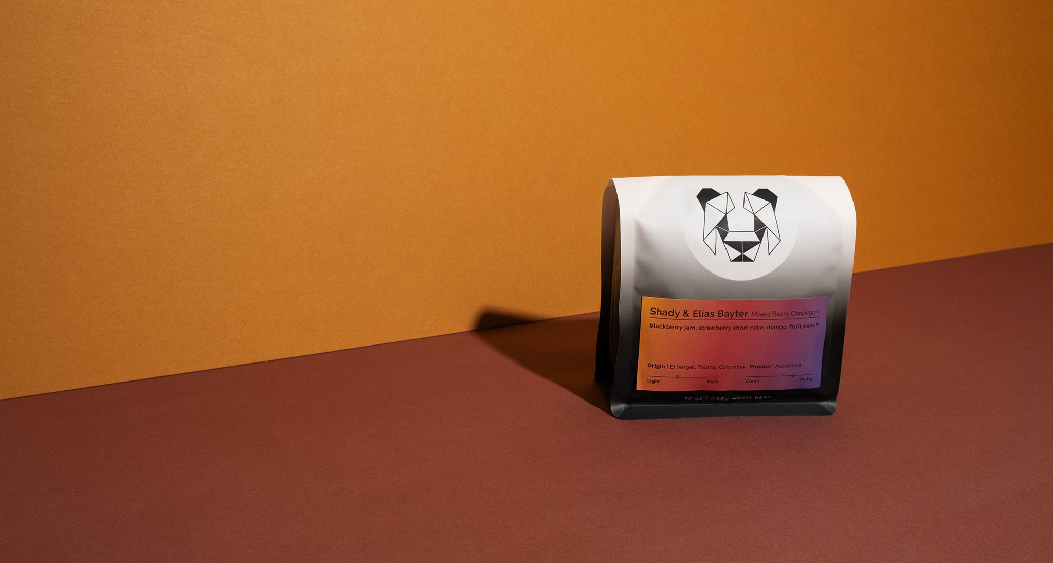 A bag of coffee on a colored backdrop with the words, "Shady and Elias Bayter Mixed Berry Ombligon" written on it. It has the tasting notes of blackberry jam, strawberry short cake, mango and fruit punch. The origin is El Vergel, Tolima, Colombia and advanced fermentation.
