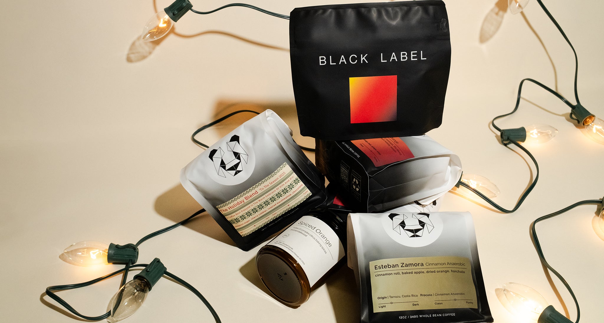 Stack of coffee bags and candles on a holiday themed backdrop with Christmas lights.