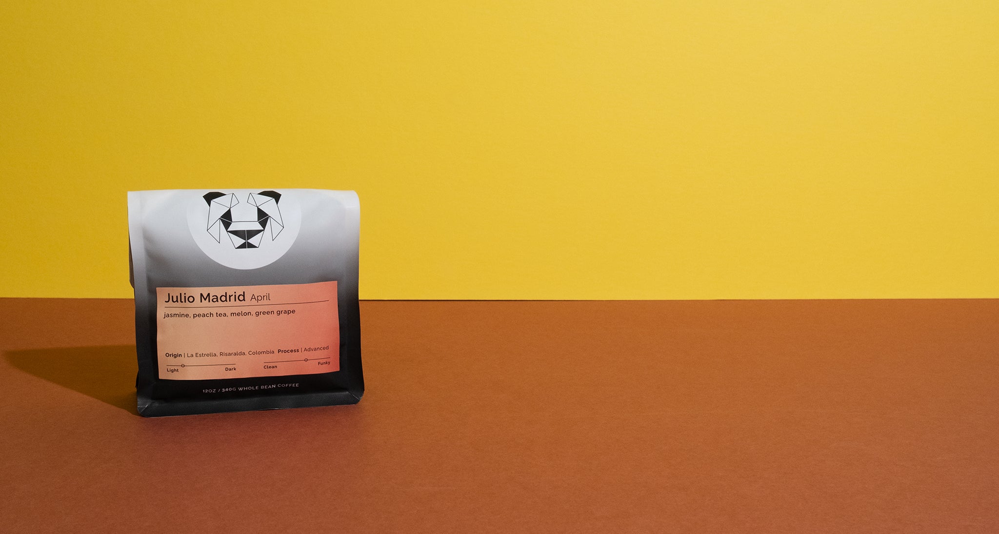 A bag of coffee with a panda logo on the front on a colorful backdrop. The coffee label says Julio Madrid April with tasting notes of jasmine, peach tea, melon and green grape.