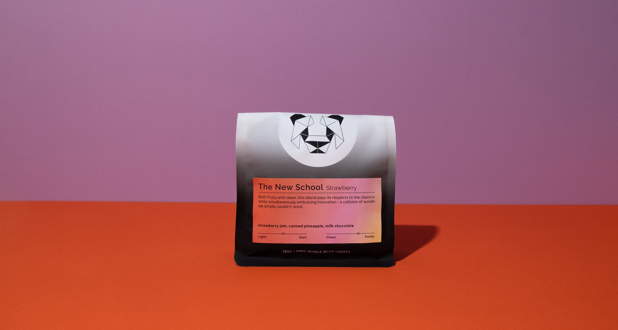 A single packaged coffee bag stands upright on a bright orange surface against a purple background. The package is mostly black with a white panda logo near the top and a peach-colored label reading 'The New School Strawberry.