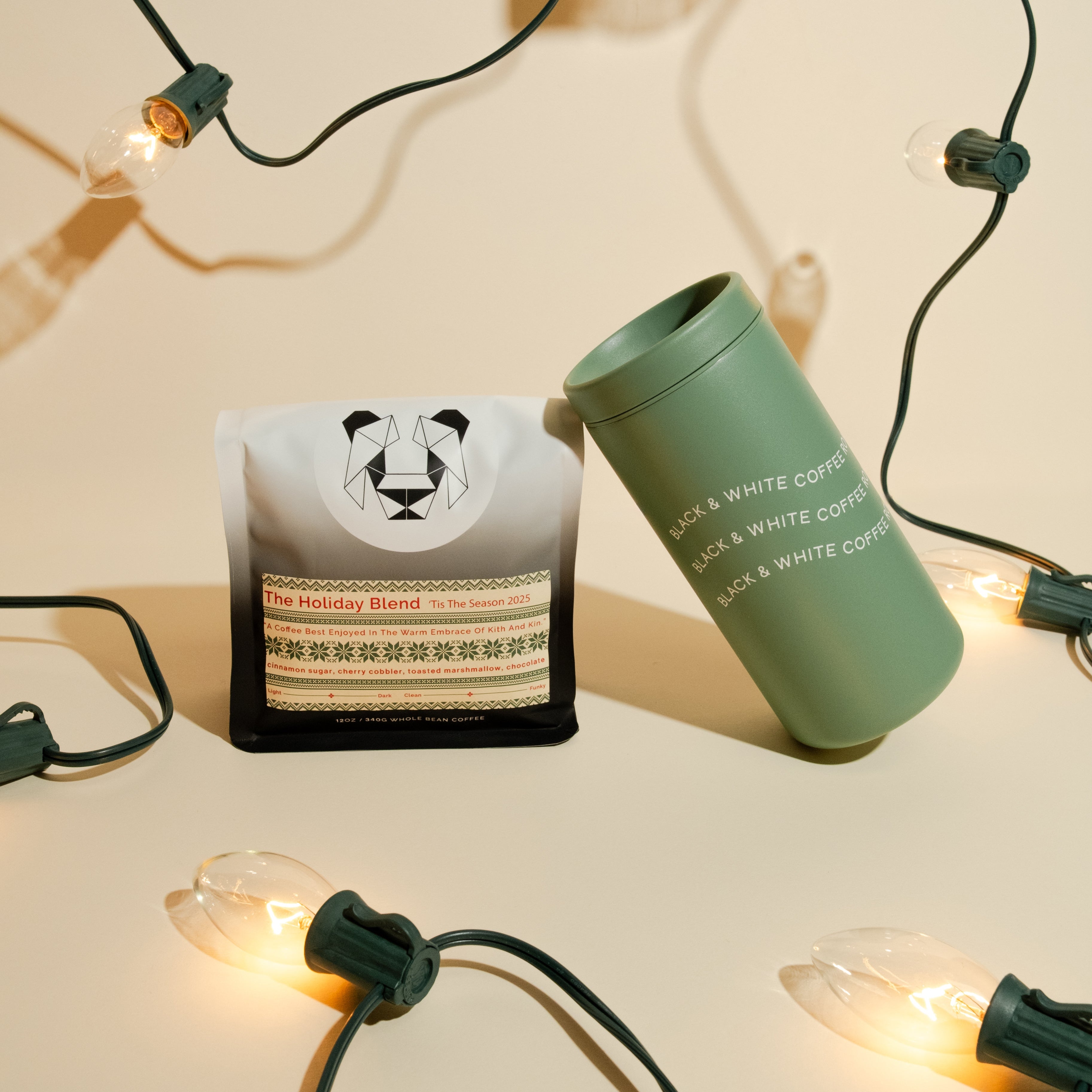 Holiday Blend Travel Set featuring a 12 oz bag of whole-bean coffee with festive flavors and a branded matte green travel tumbler, framed by string lights.