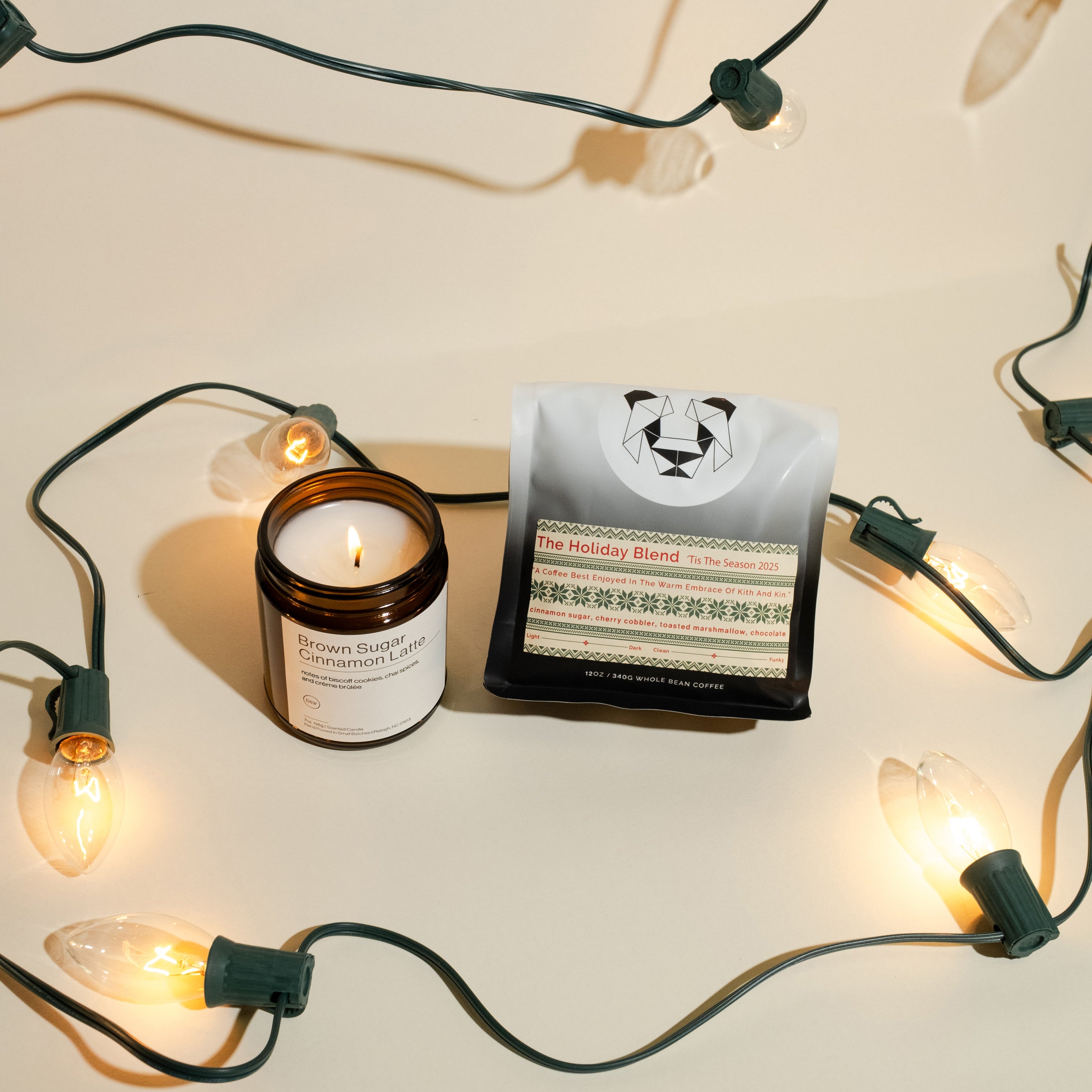 Holiday Blend Candle Set featuring a lit amber glass jar candle and a 12 oz bag of whole-bean coffee, adorned with warm white holiday lights.