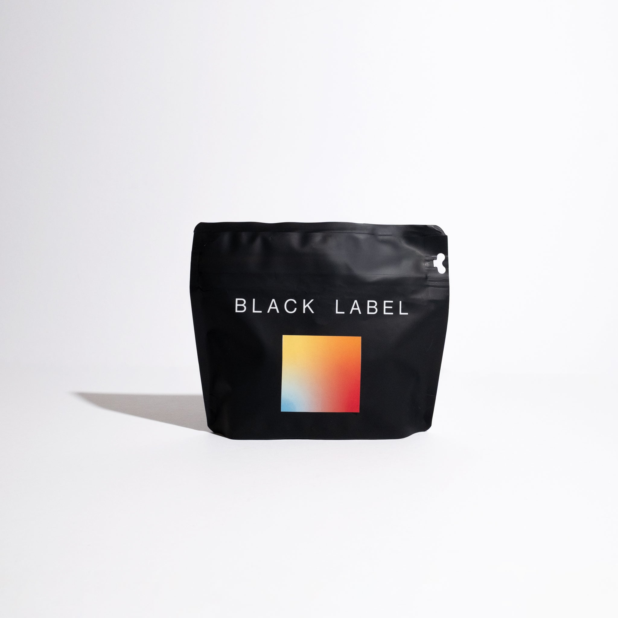 Matte-black pouch labeled BLACK LABEL, featuring gradient square graphic, represents Janson Natural Gesha - Lot 914, highlighting Janson Farms' coffee legacy.