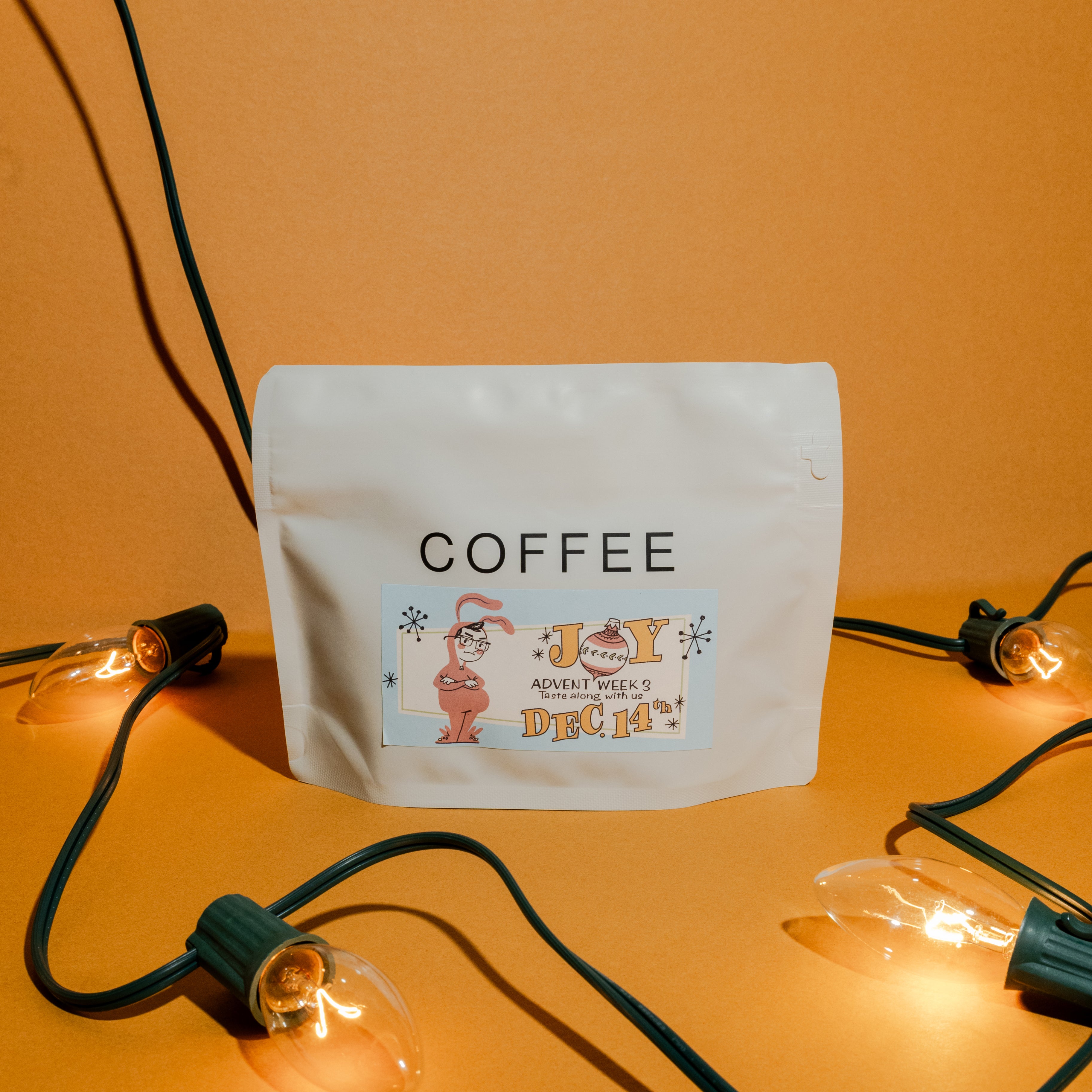 2025 B&W Advent Calendar coffee pouch, labeled “COFFEE,” features a holiday sticker with a bunny, set against vintage-style lightbulbs.