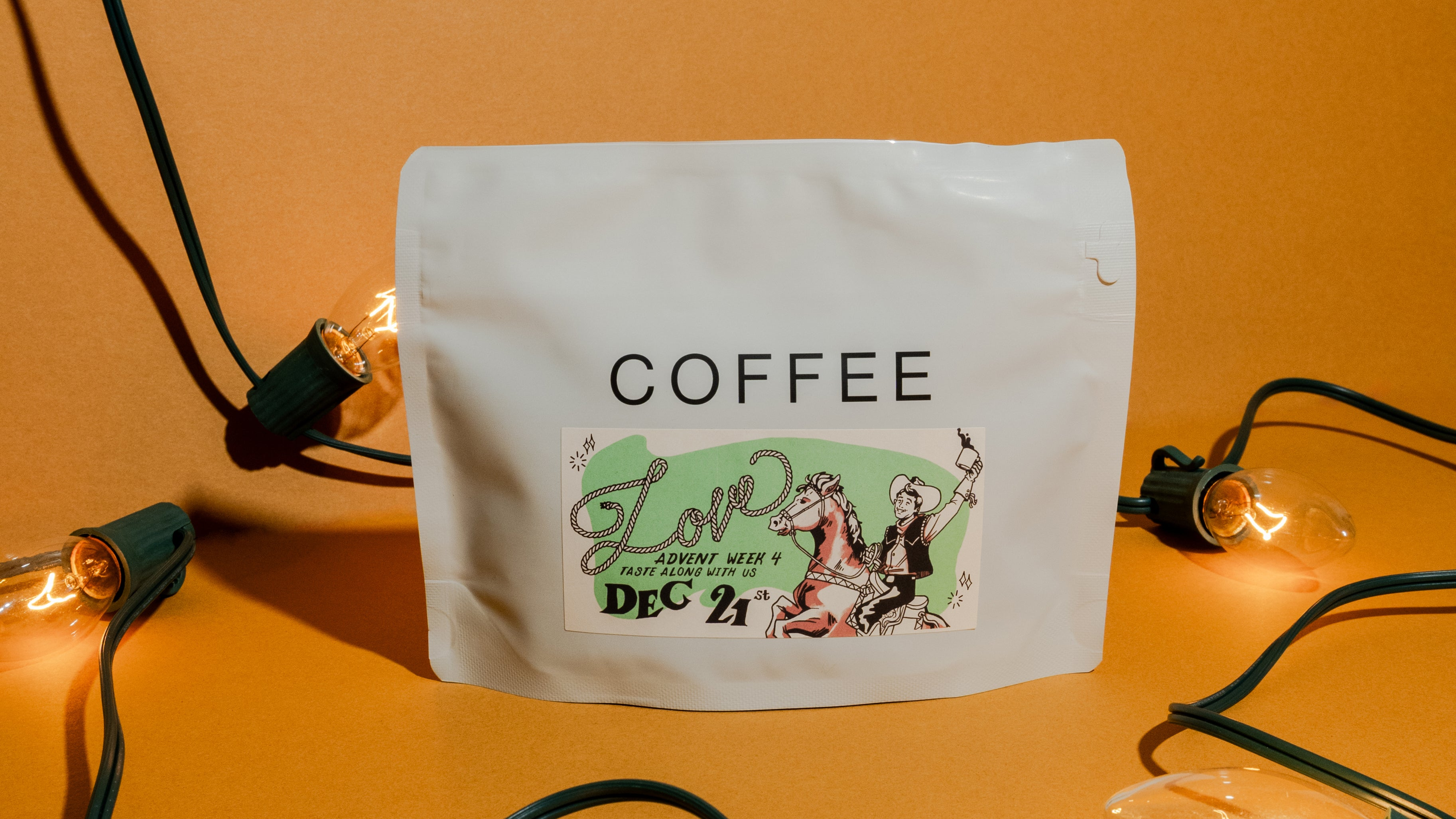 2025 B&W Advent Calendar coffee pouch with holiday sticker, surrounded by lit string lights, inviting tasting on December 21st.