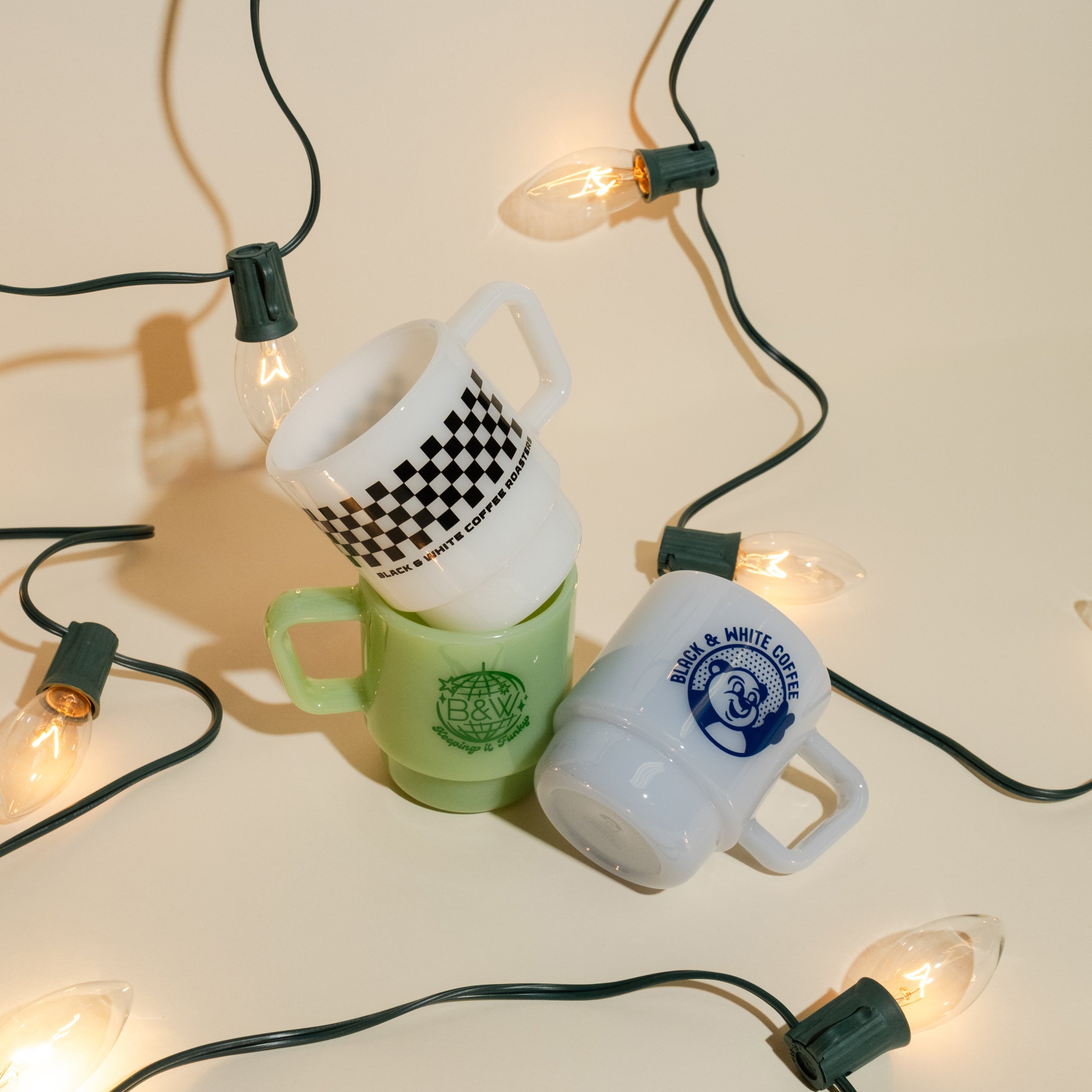 Stack of milk glass mugs on a holiday themed backdrop with festive lights.