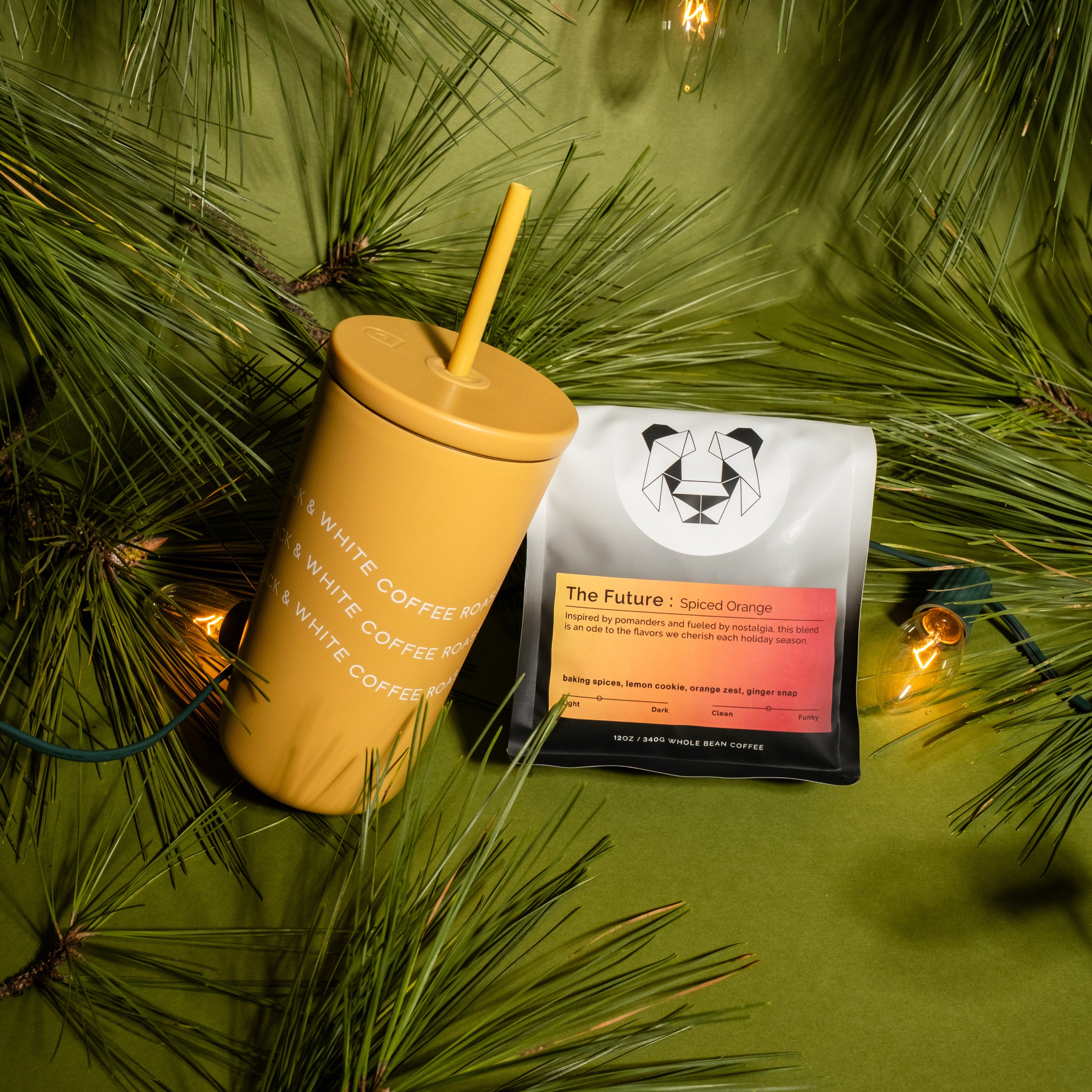 Spiced Orange Travel Set featuring a mustard-yellow tumbler and The Future: Spiced Orange coffee bag with festive pine needles and glowing string lights.