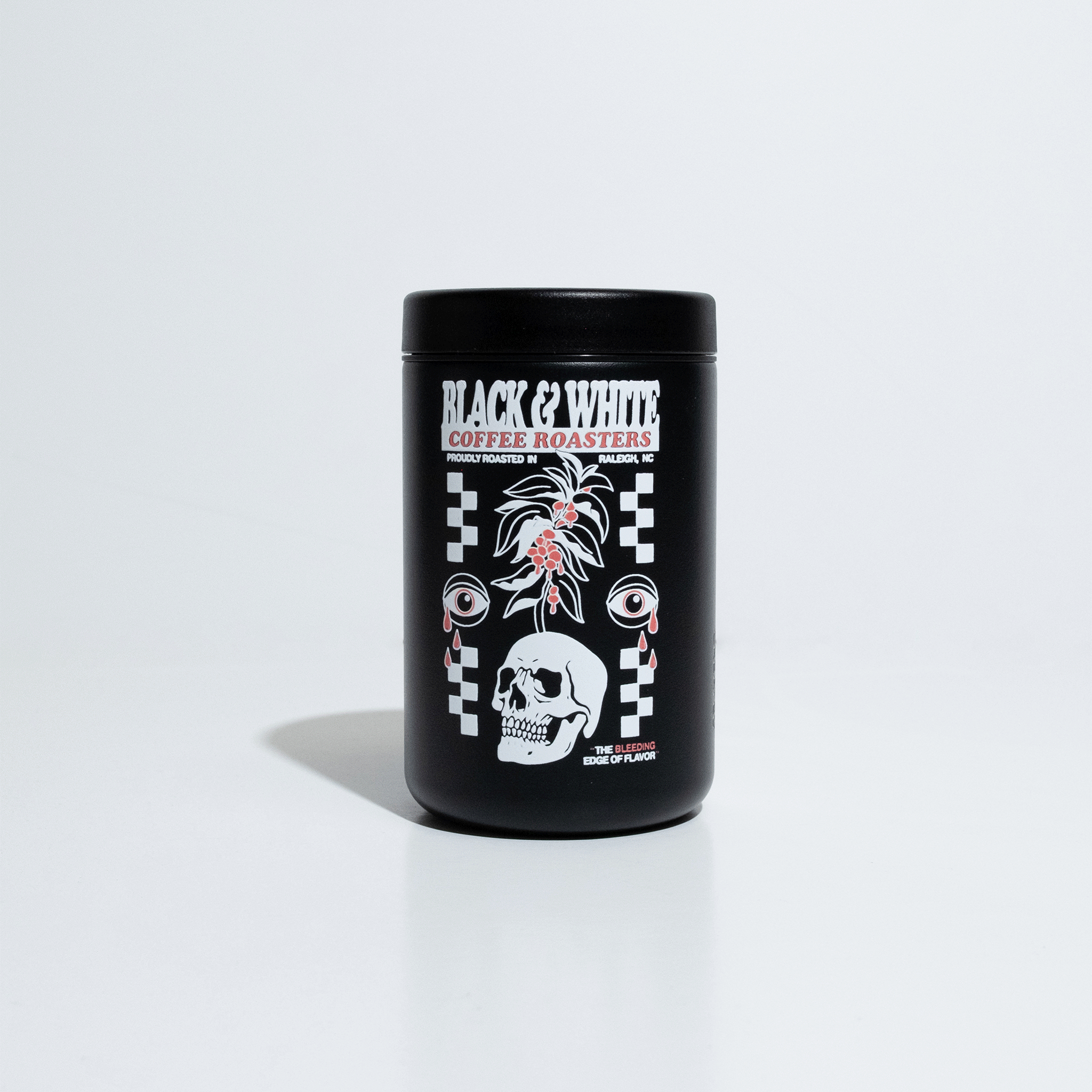 A Black 10oz travel cup with a large white and red graphic that says, "Black and White Coffee Roasters, Proudly roasted in Raleigh, NC" and "The Bleeding Edge Of Flavor." The graphic has checker board design on the left and right with a skull with a coffee tree growing out of it. The graphic is finished off two eyeballs crying red tear drops. The cup is turning to show all sides of the cup.